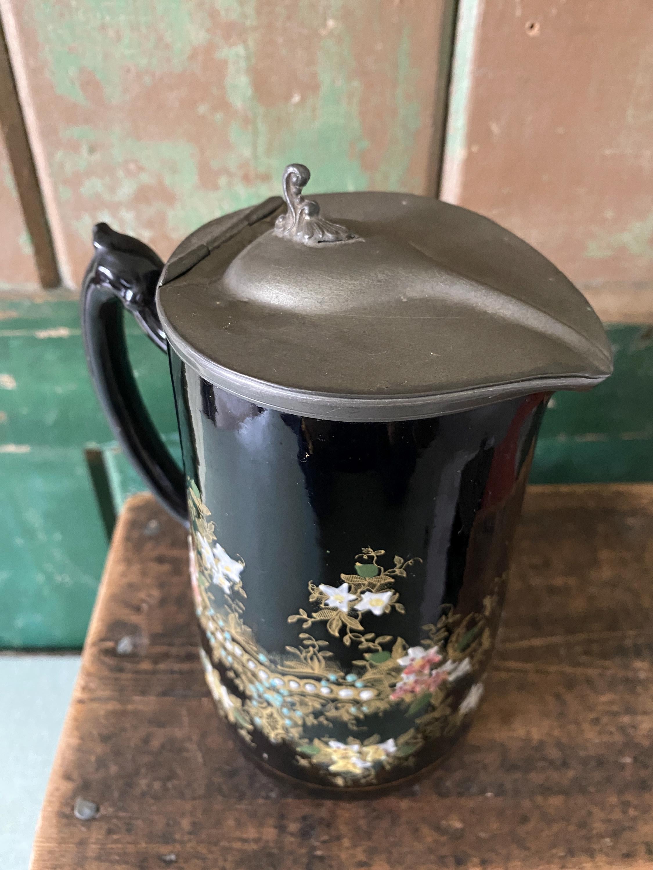 Top view of a decorative black jug with floral patterns and a metal lid 