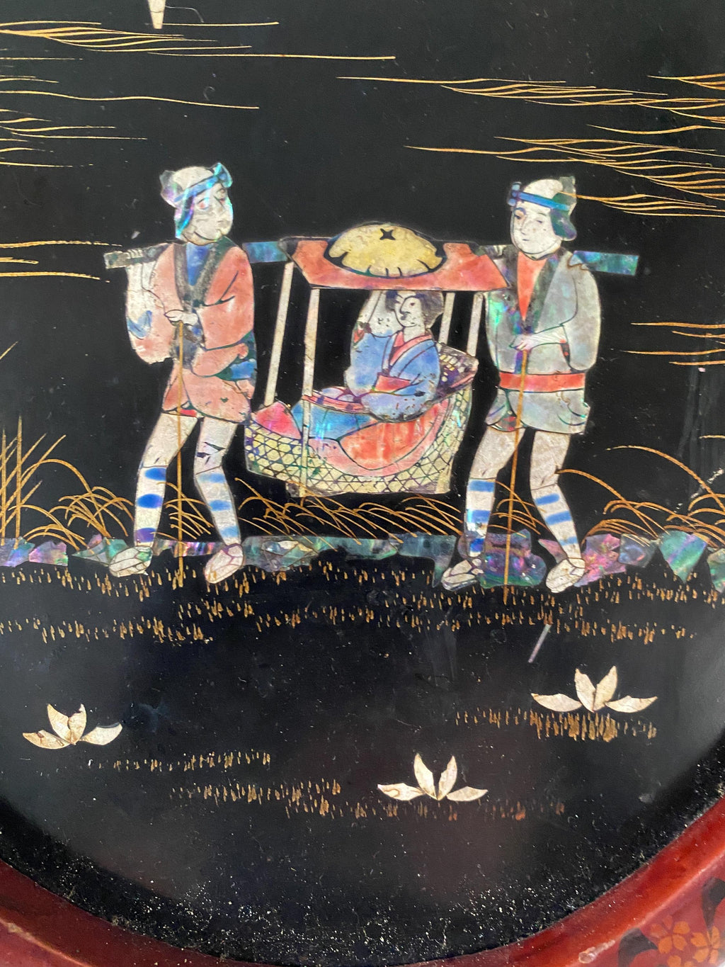 Detail of a decorative panel with a design of a woman being carried in a sedan chair by two male figures on a black background