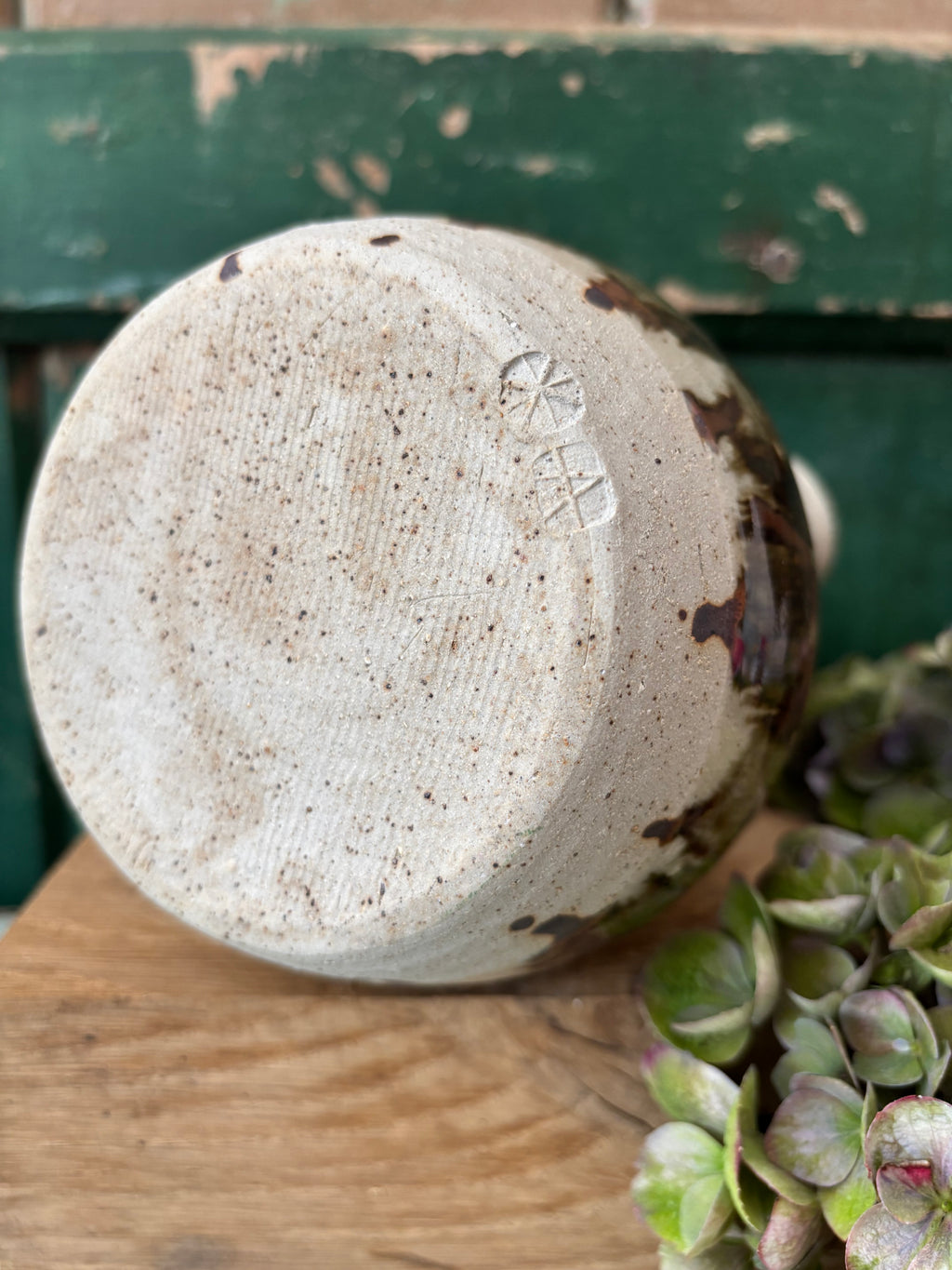 A handmade ceramic vase with a textured, speckled off-white glaze and dark brown accents, showing the maker's mark underneath.