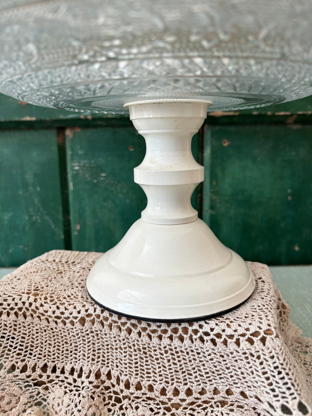 A vintage cream enamel pedestal stand with a flared base, shown holding a clear glass plate.