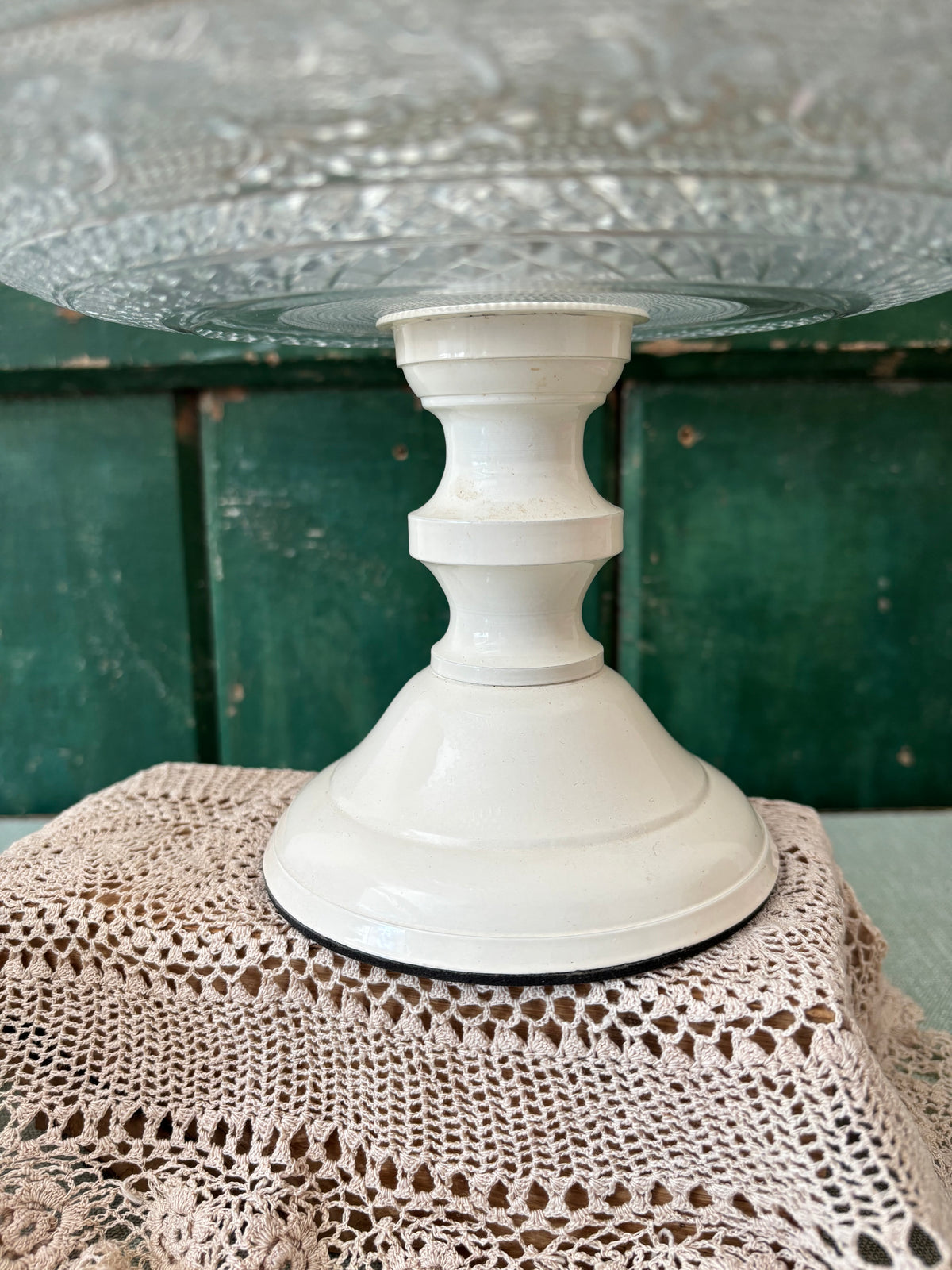 A vintage cream enamel pedestal stand with a flared base, shown holding a clear glass plate.