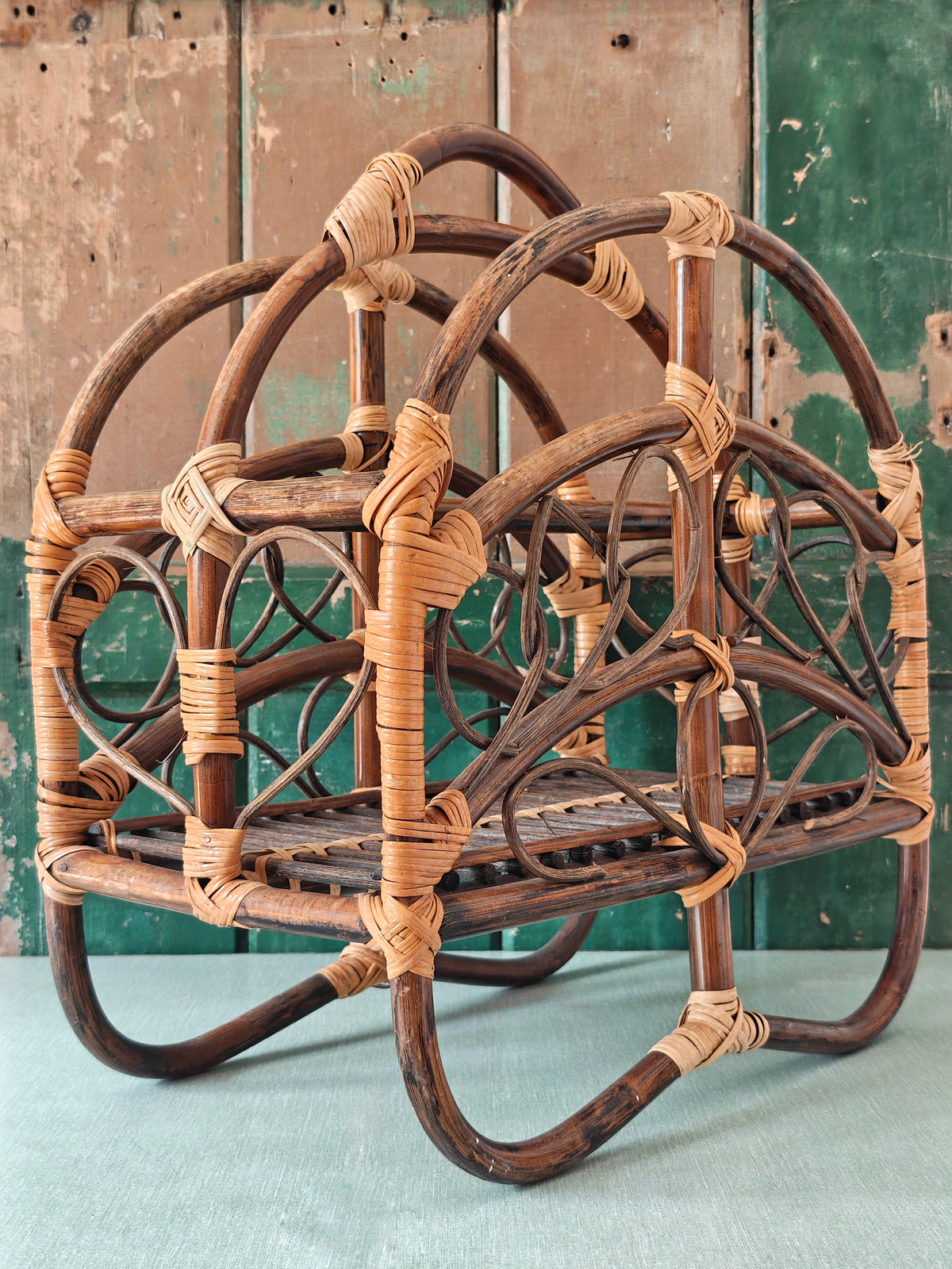 A vintage bamboo and rattan magazine rack with a rounded dome shape, featuring brown wooden frame and woven bamboo accents.