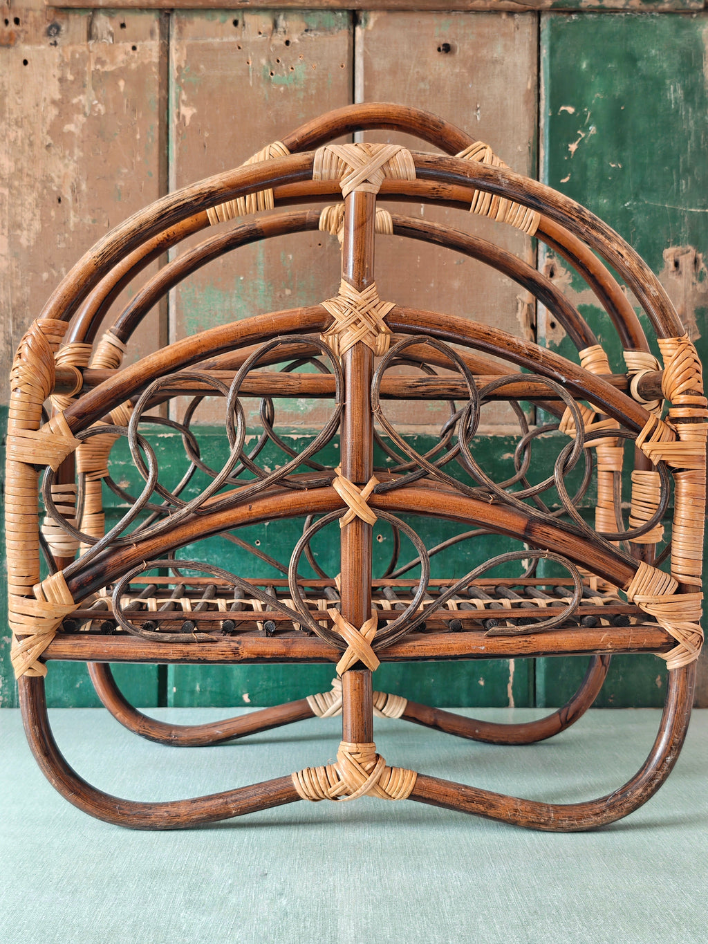 A vintage bamboo and rattan magazine rack with a rounded dome shape, featuring brown wooden frame and woven bamboo accents.