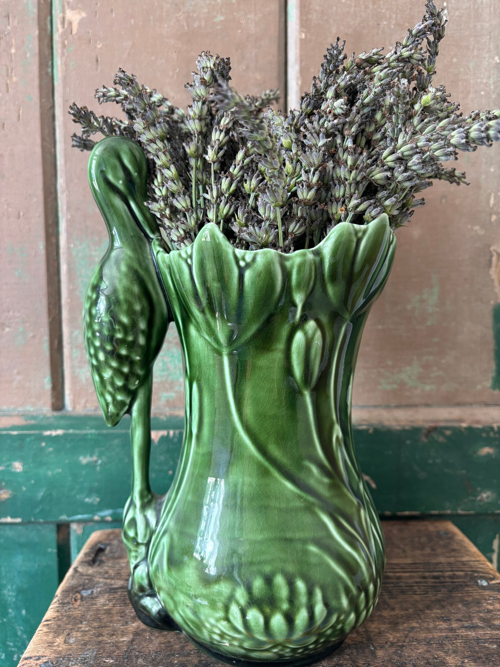 A green ceramic vase shaped like a lotus flower, featuring a sculpted heron on the side.