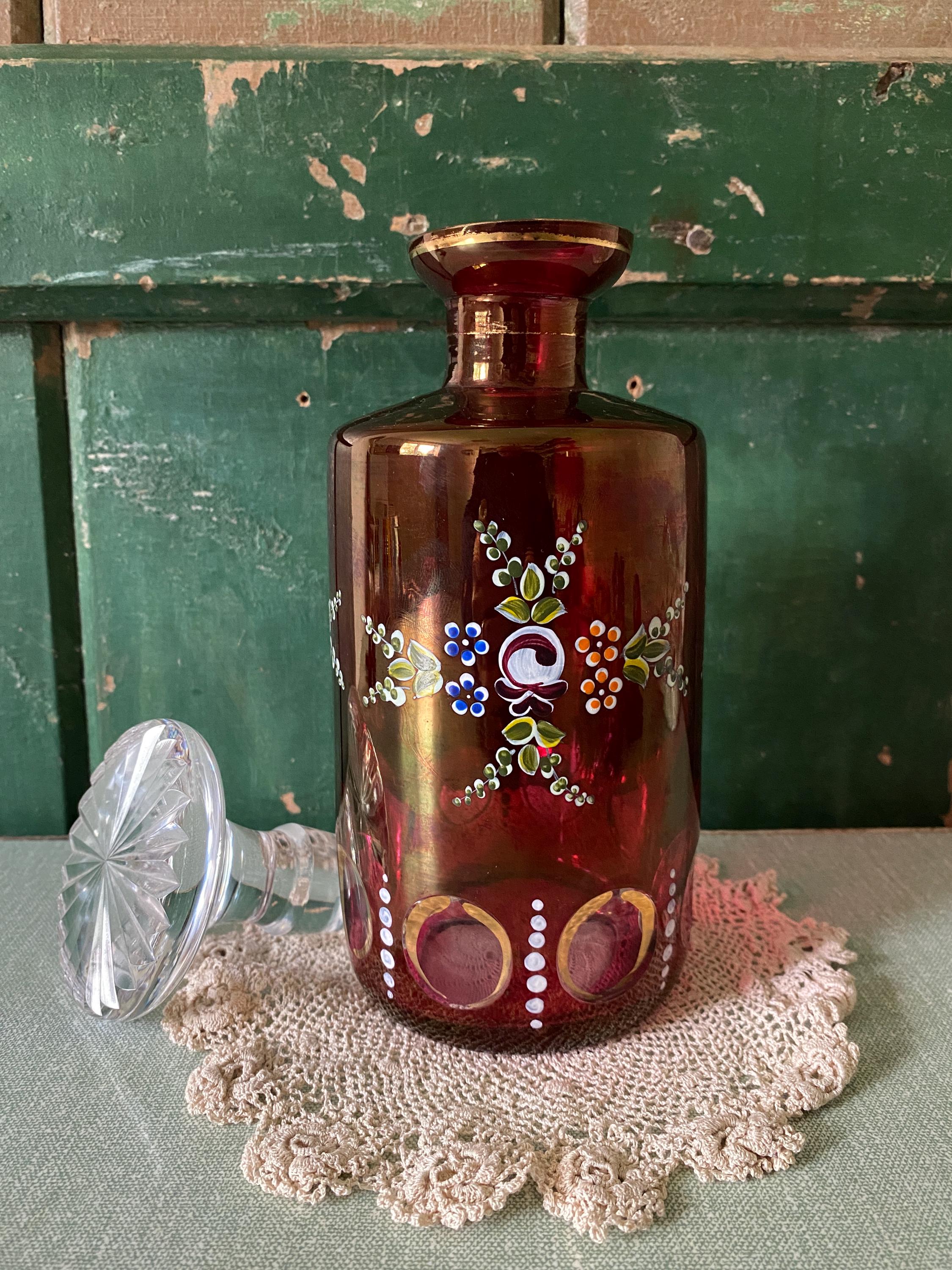 Decorative red glass bottle with floral patterns and a clear glass stopper
