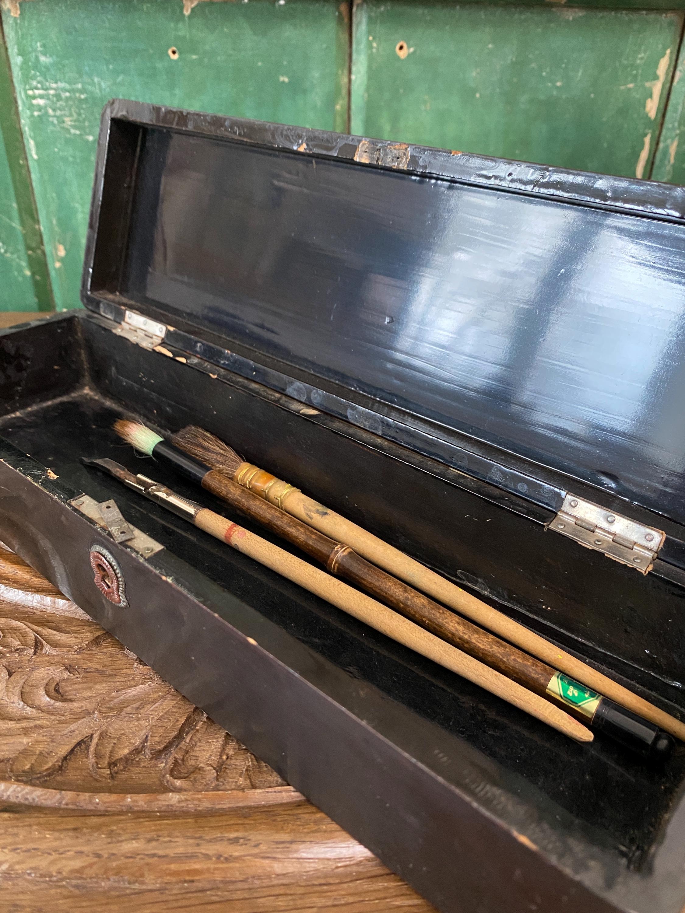 A black lacquered box open with paint brushes
