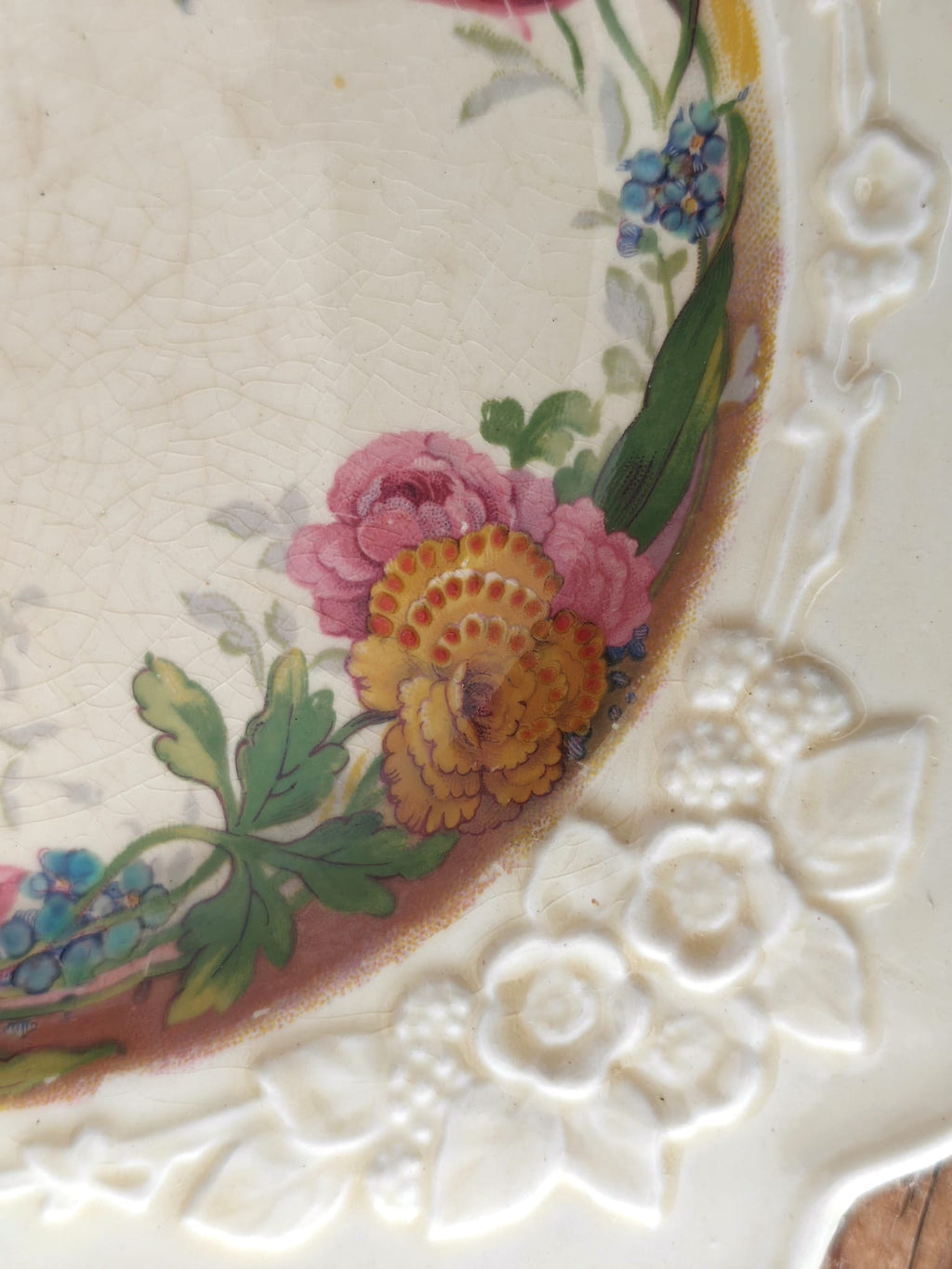 Close-up of an antique ceramic plate corner showing a cream embossed floral border and painted flowers.