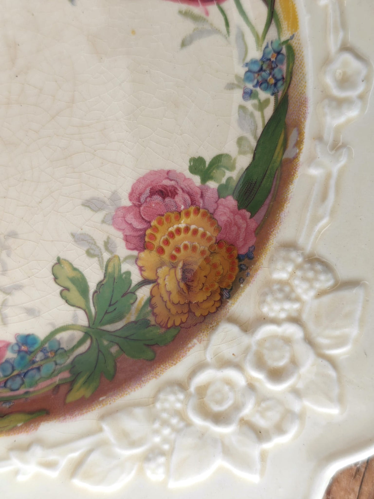 Close-up of an antique ceramic plate corner showing a cream embossed floral border and painted flowers.