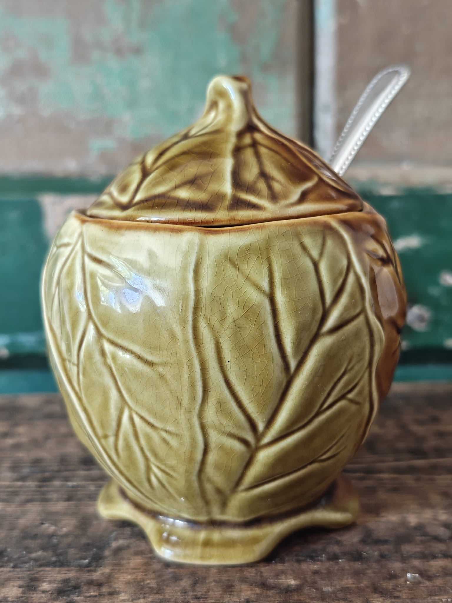 A ceramic lidded container with a leaf-like embossed pattern in a warm olive-gold glaze.