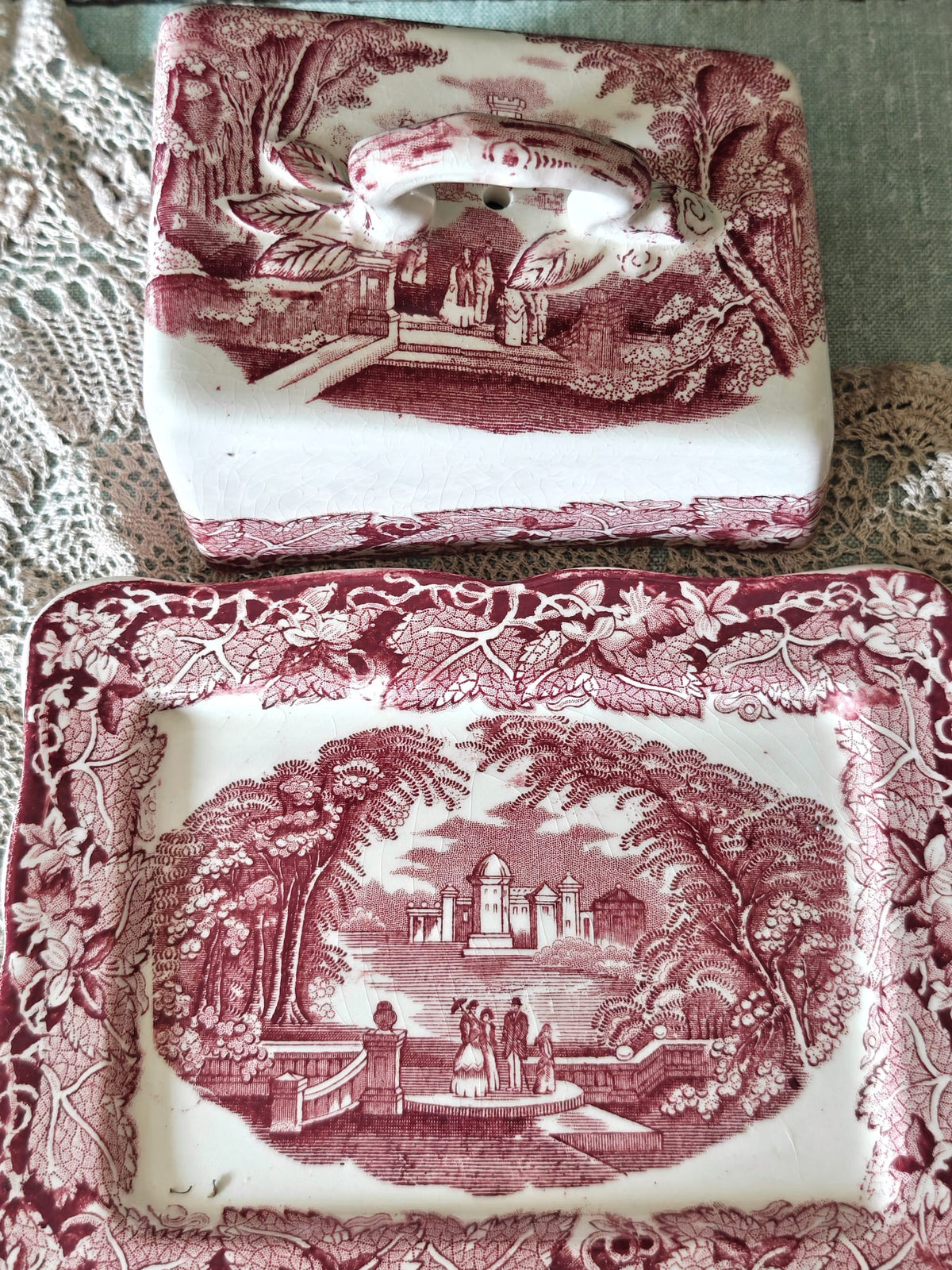 A Masons Vista butter dish and matching lid set with a pink and white transfer pattern depicting a classical landscape scene with figures and trees.