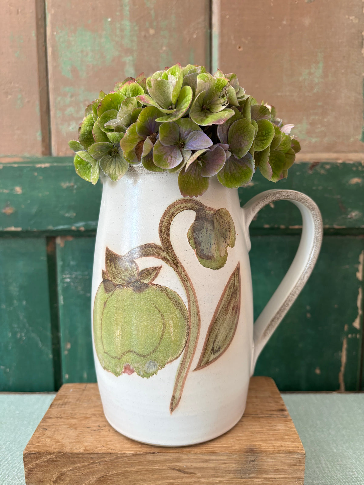 A white ceramic pitcher vase decorated with a green and brown botanical illustration.