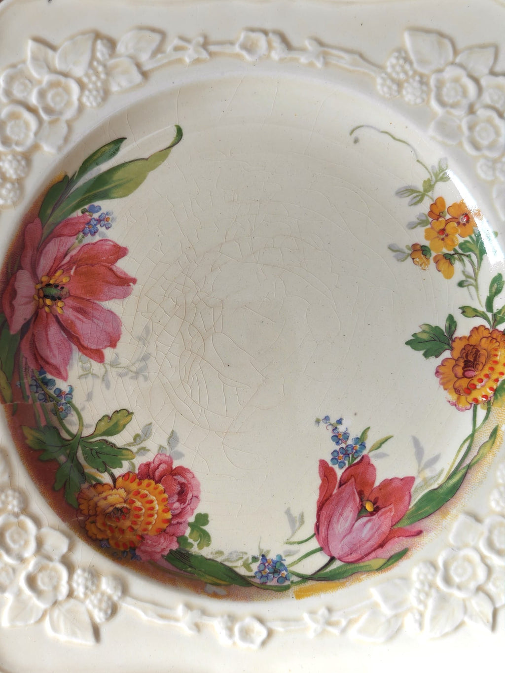 A vintage ceramic plate with an embossed floral border and a hand-painted floral design in the centre.
