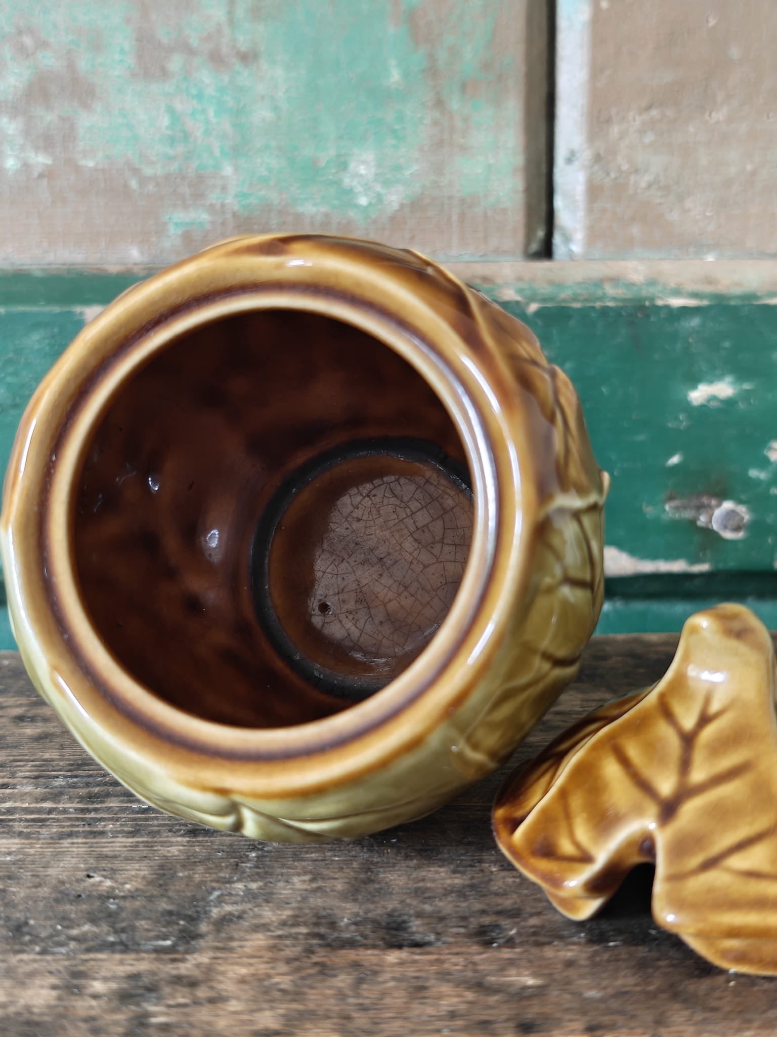 A ceramic lidded container with a leaf-like embossed pattern in a warm olive-gold glaze, with the lid by the side showing an interior view of the pot.
