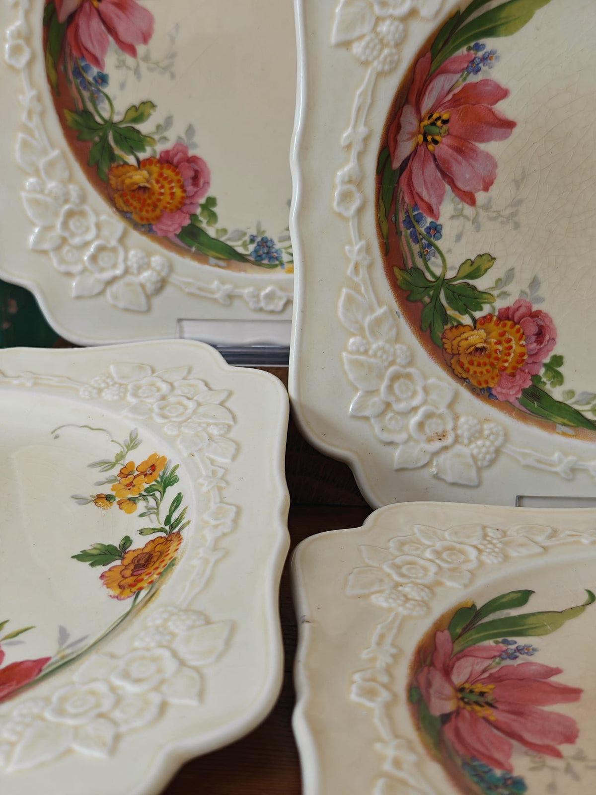 A close-up of several vintage white ceramic plates with embossed floral borders and painted floral designs in pink.