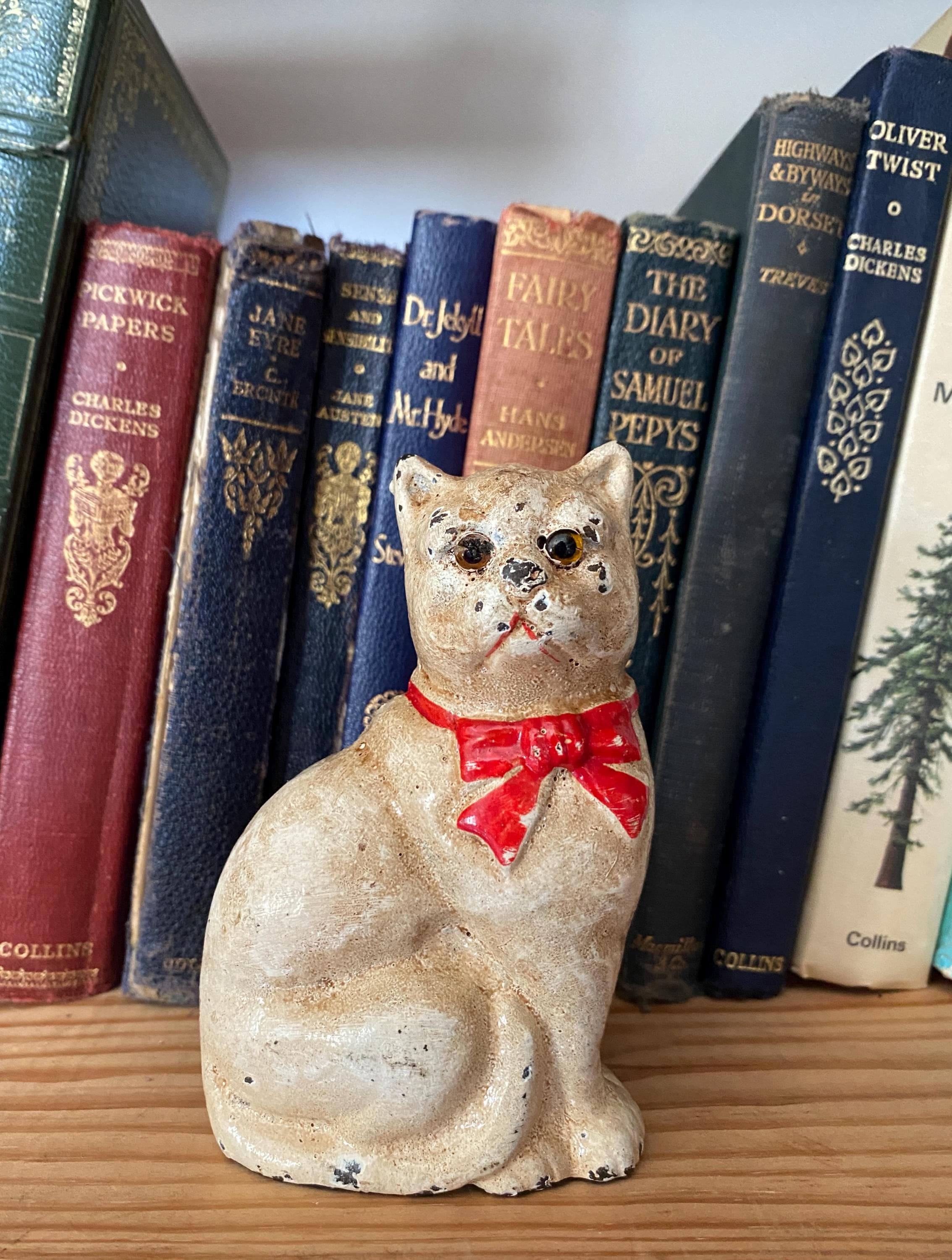 Small figurine of a white cat  with a red bow on a shelf with books