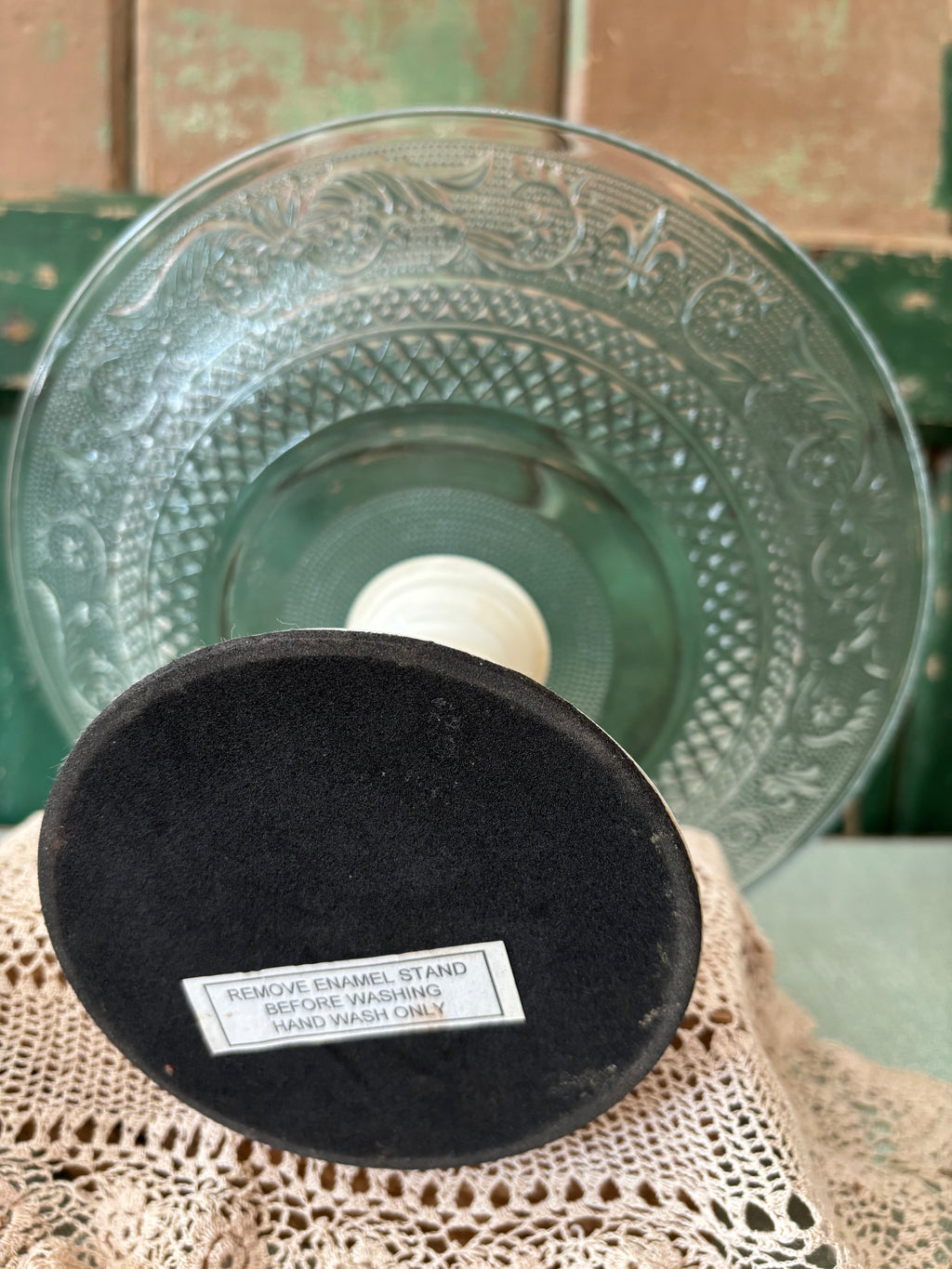 A round clear glass plate with enamel stand shown from underneath.