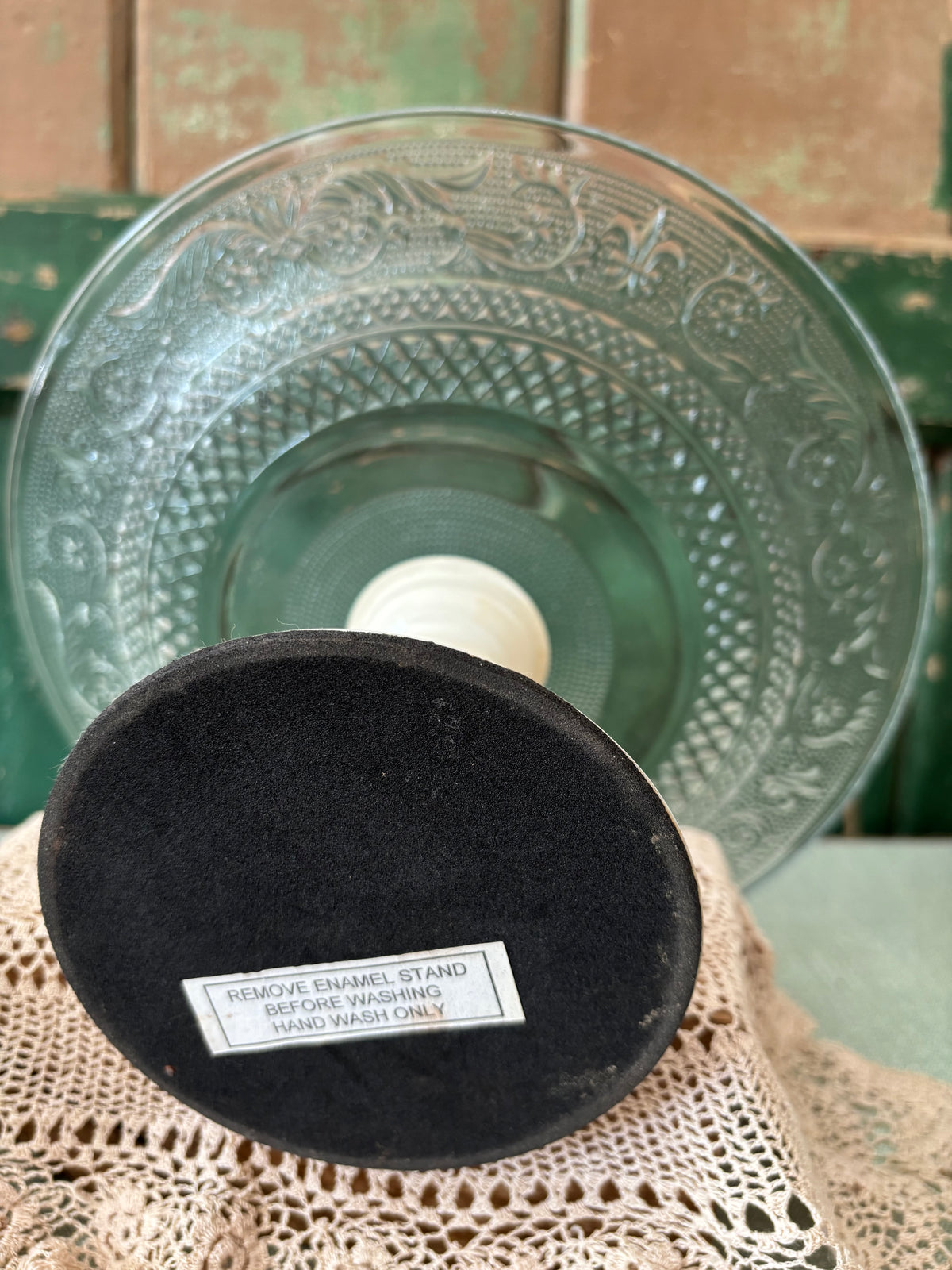 A round clear glass plate with enamel stand shown from underneath.