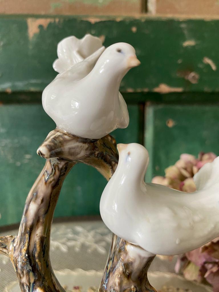 Two white ceramic doves on a branch with a green wooden background
