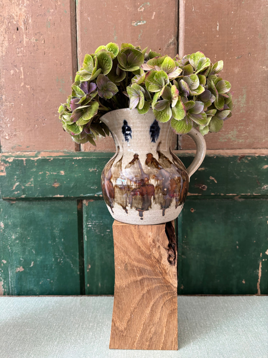 A ceramic pitcher vase with a rustic hand-painted design,.