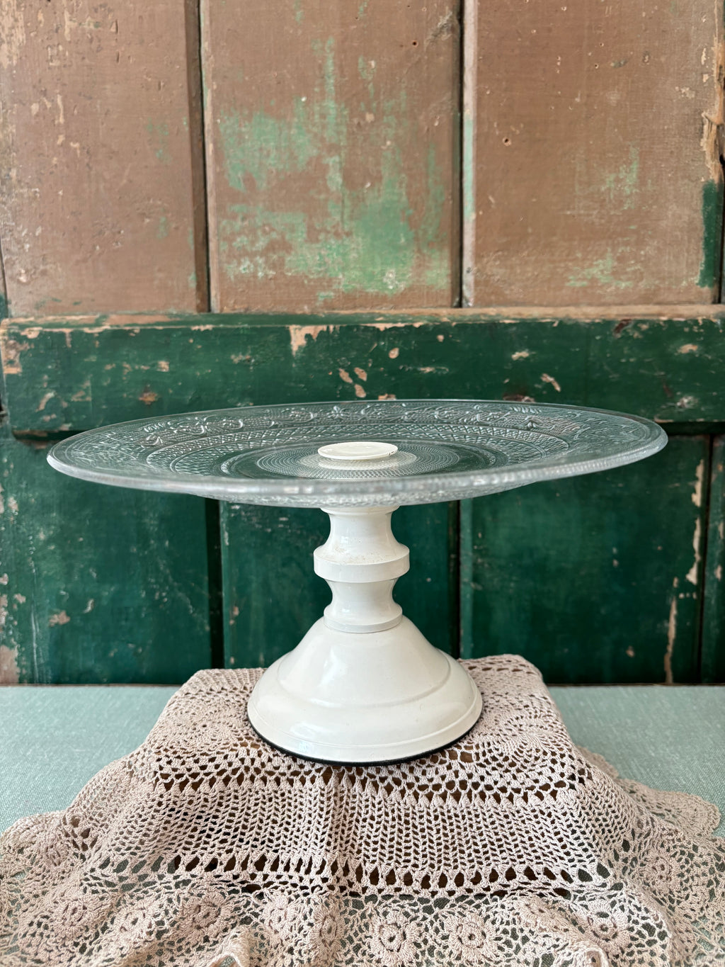 A vintage cream pedestal cake stand with a pressed glass top.