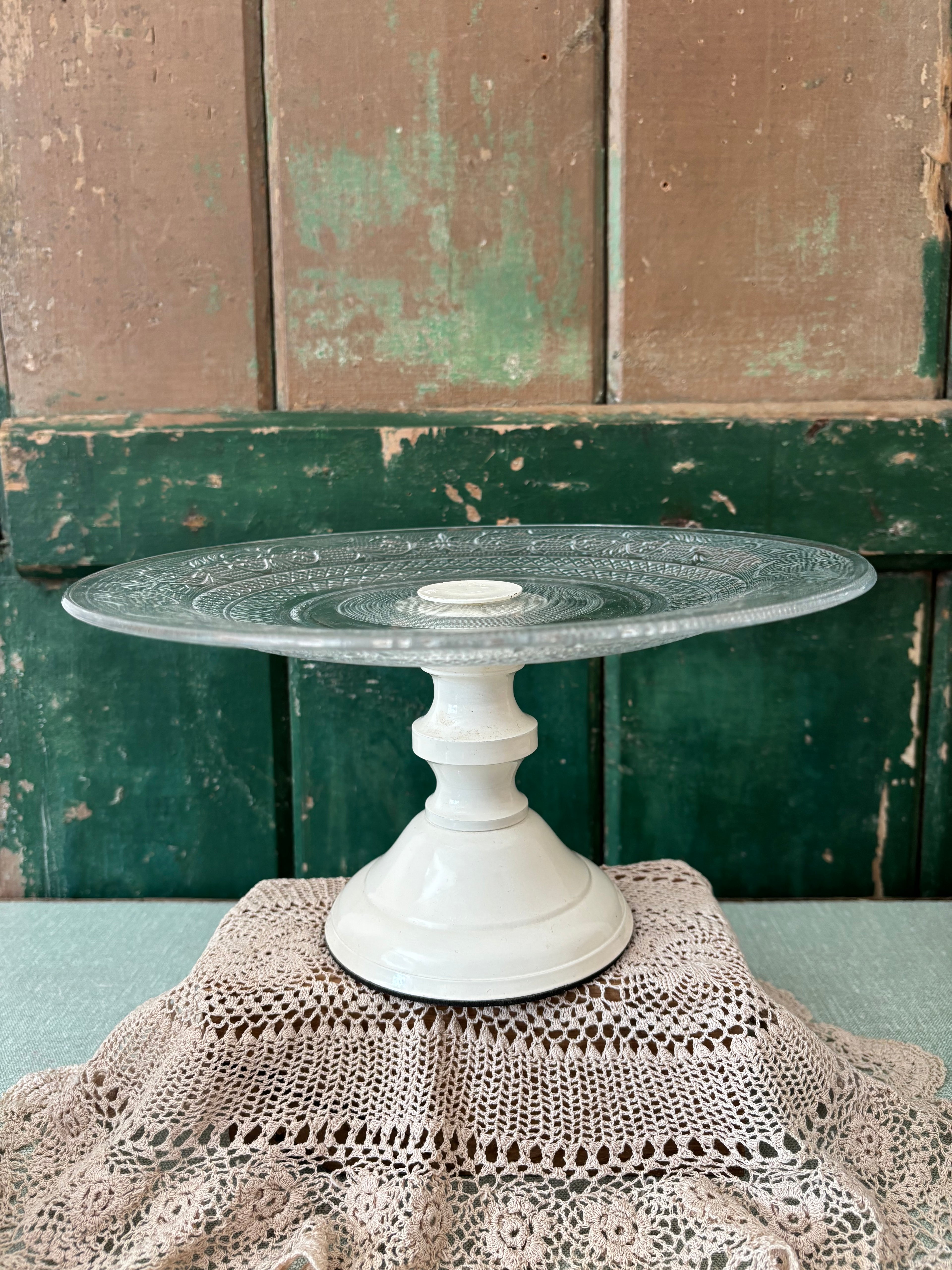 A vintage cream pedestal cake stand with a pressed glass top.