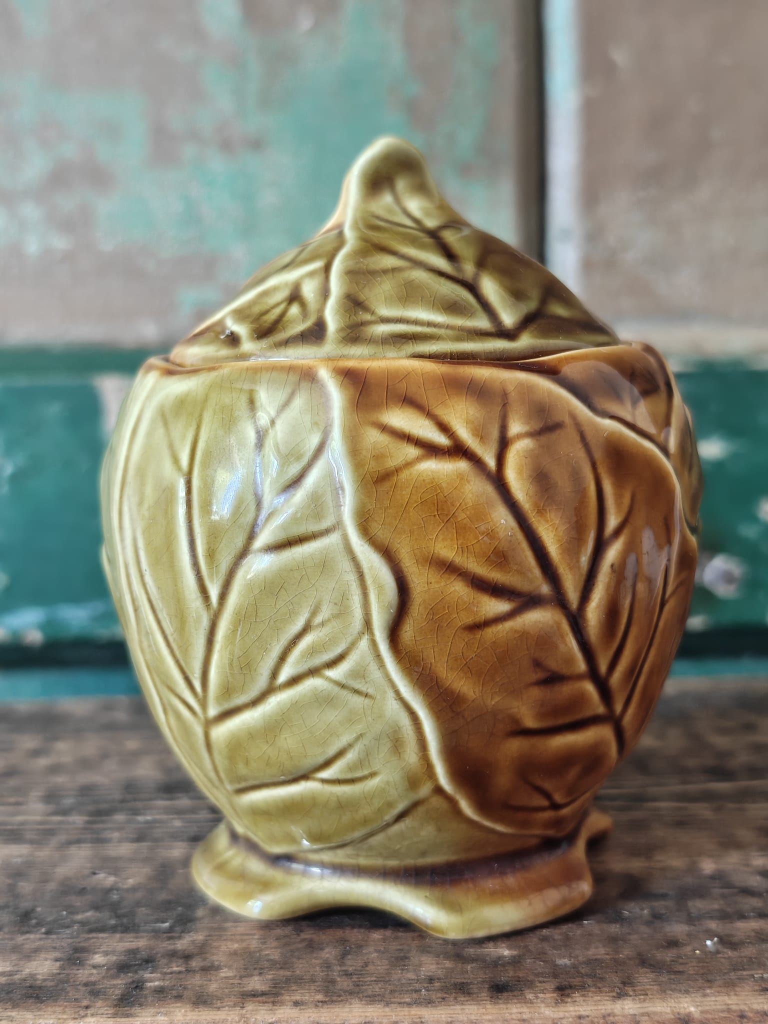 A ceramic lidded container with a leaf-like embossed pattern in a warm olive-gold glaze.