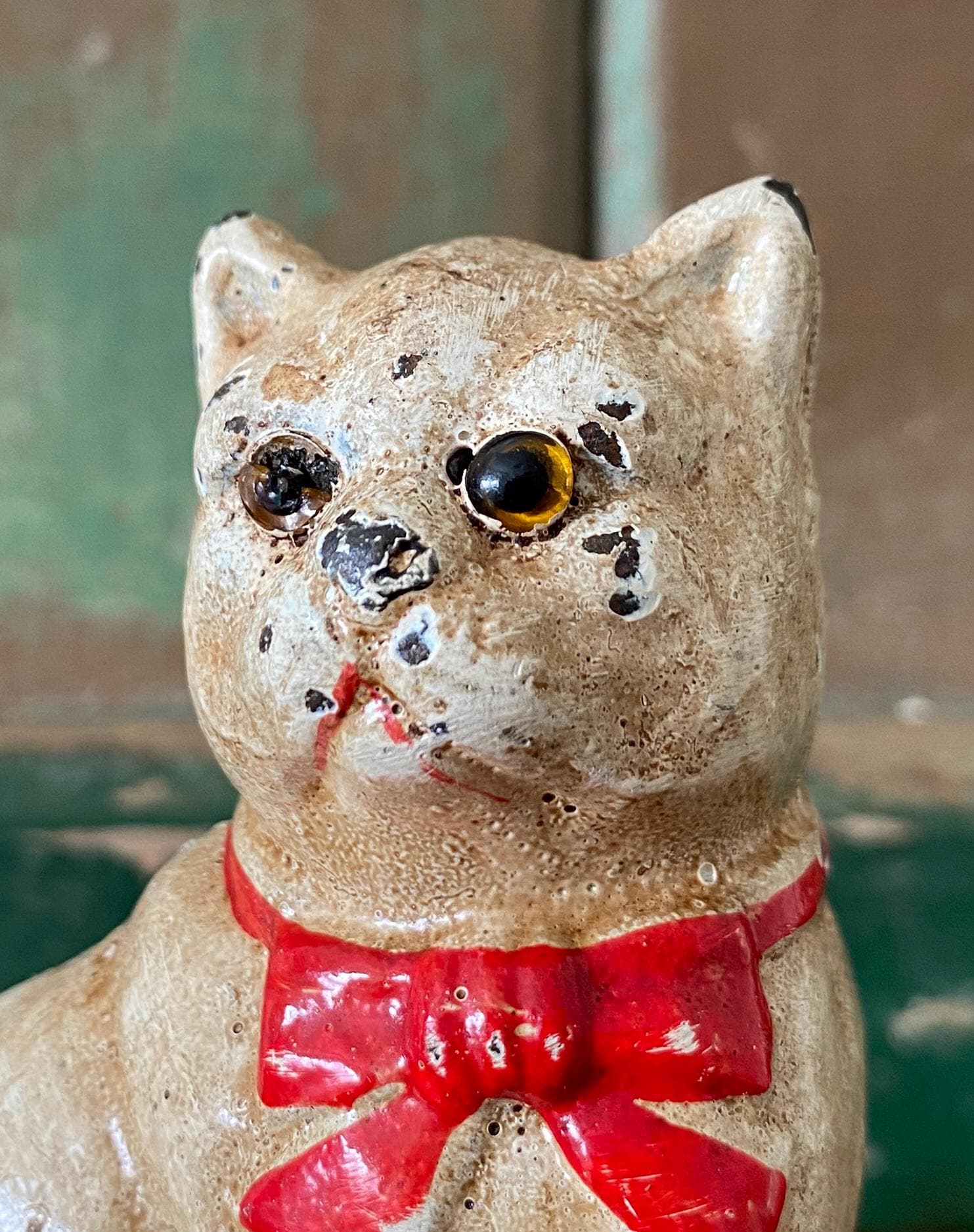 Close-up of the face of a vintage metal cat figurine with a red bow