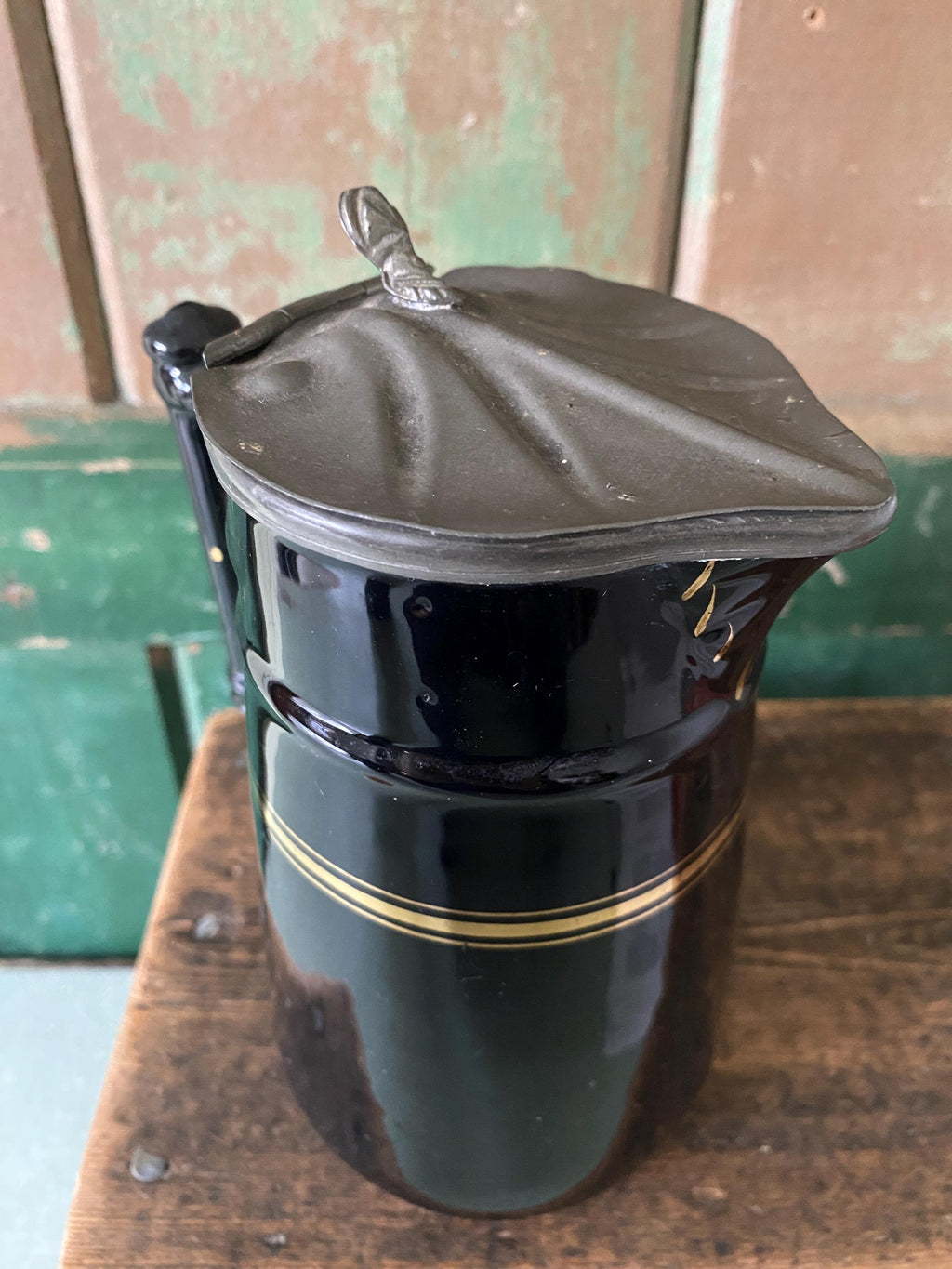 Detail of the metal lid of a black ceramic pitcher with gold stripe