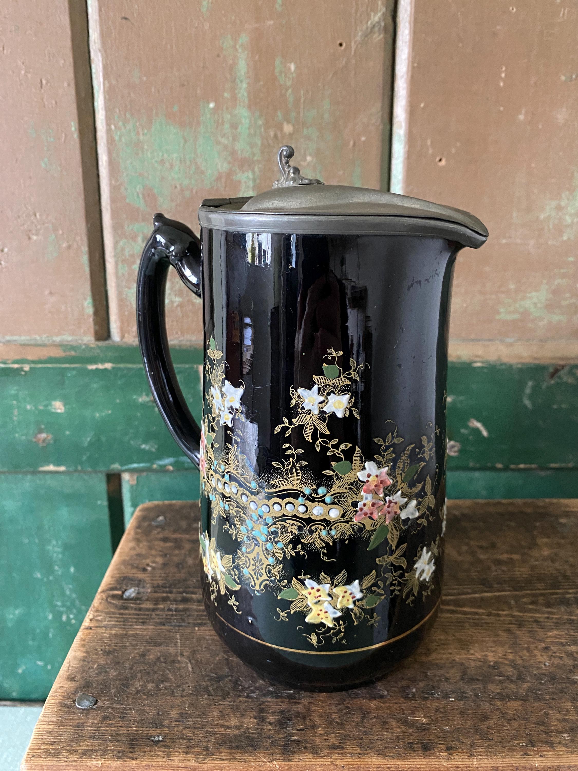 Decorative black jug with floral patterns and a metal lid 