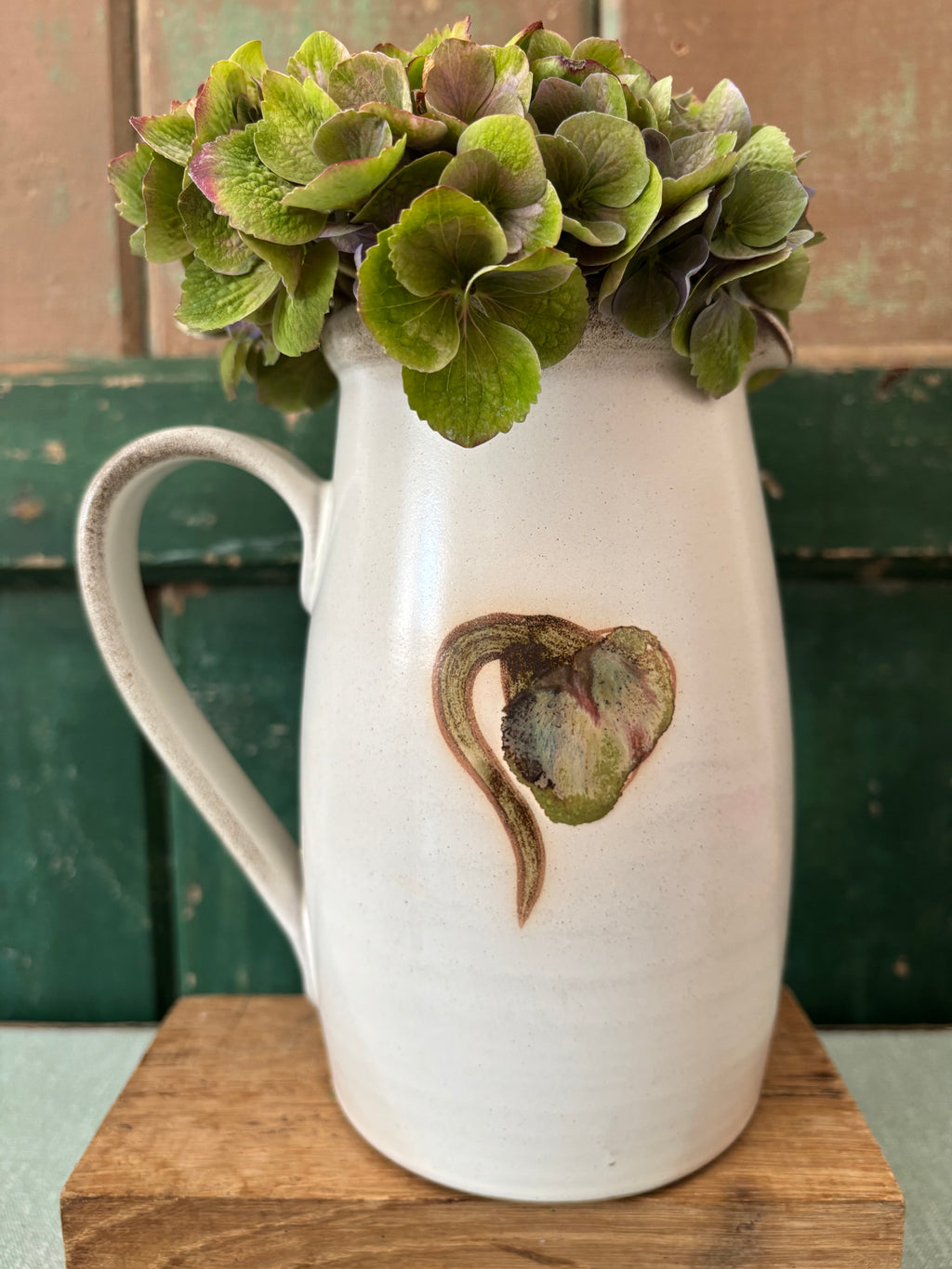 A white Denby ceramic pitcher vase with a rustic handle and a painted design.
