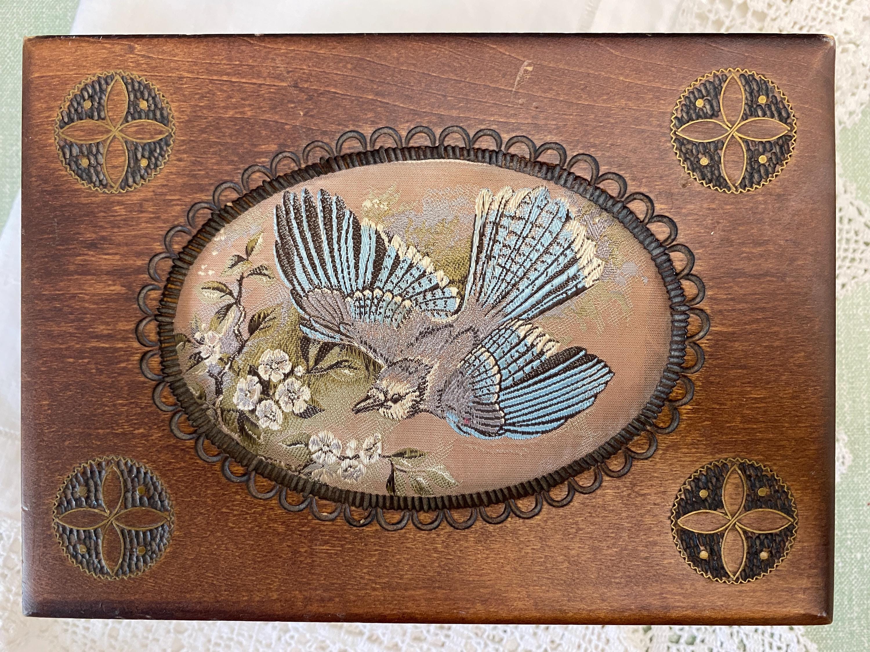 Wooden box with embroidered design of a bird and flowers on a wooden background