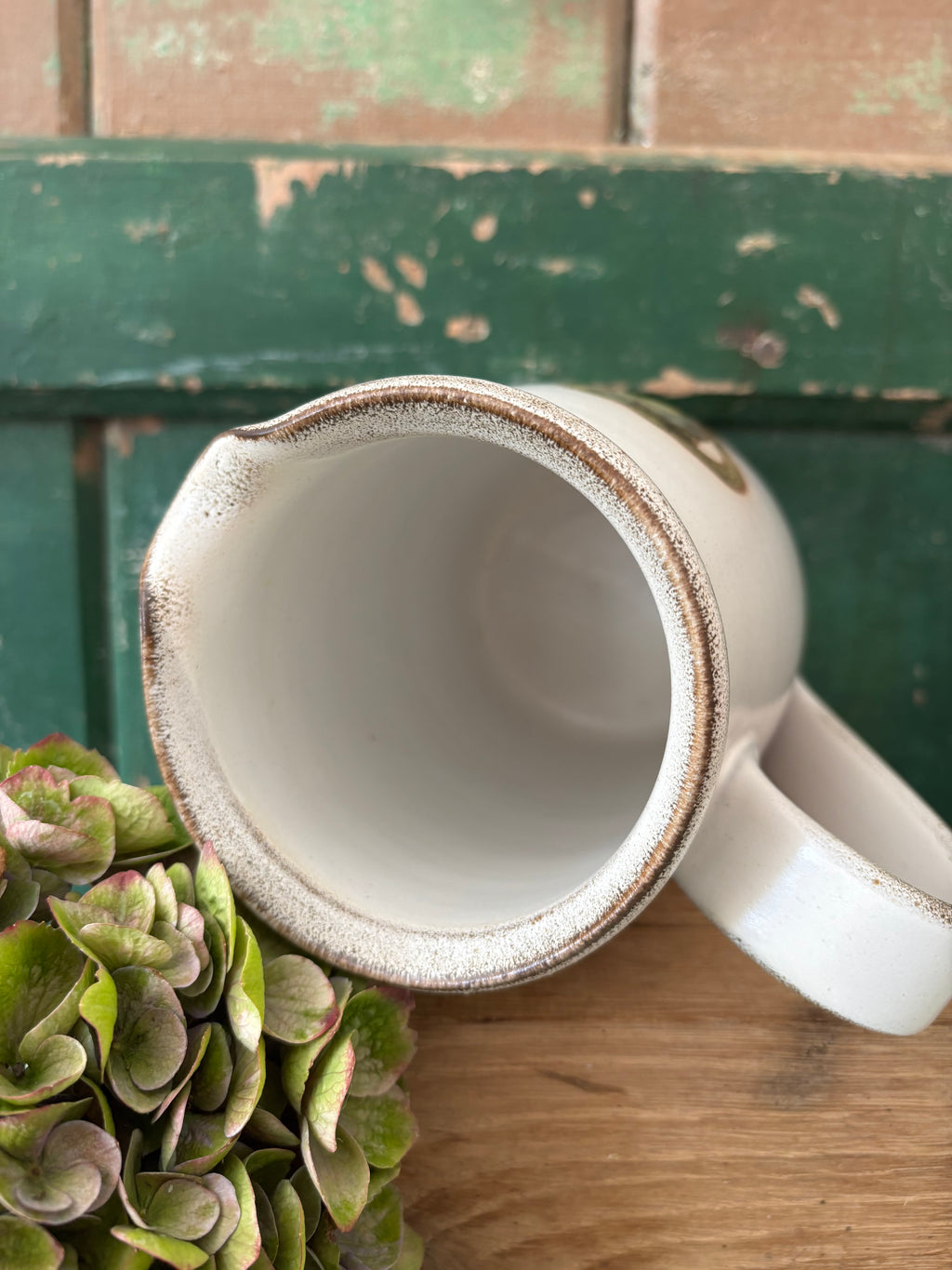 A close-up of a white ceramic pitcher with a rustic, distressed brown rim showing the interior.