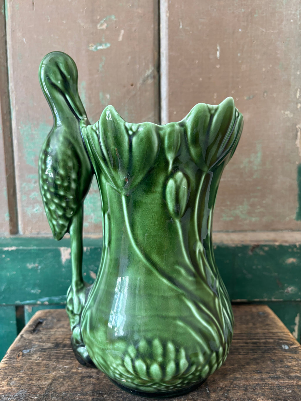A dark green ceramic vase shaped like a lotus flower with a heron perched on the side.