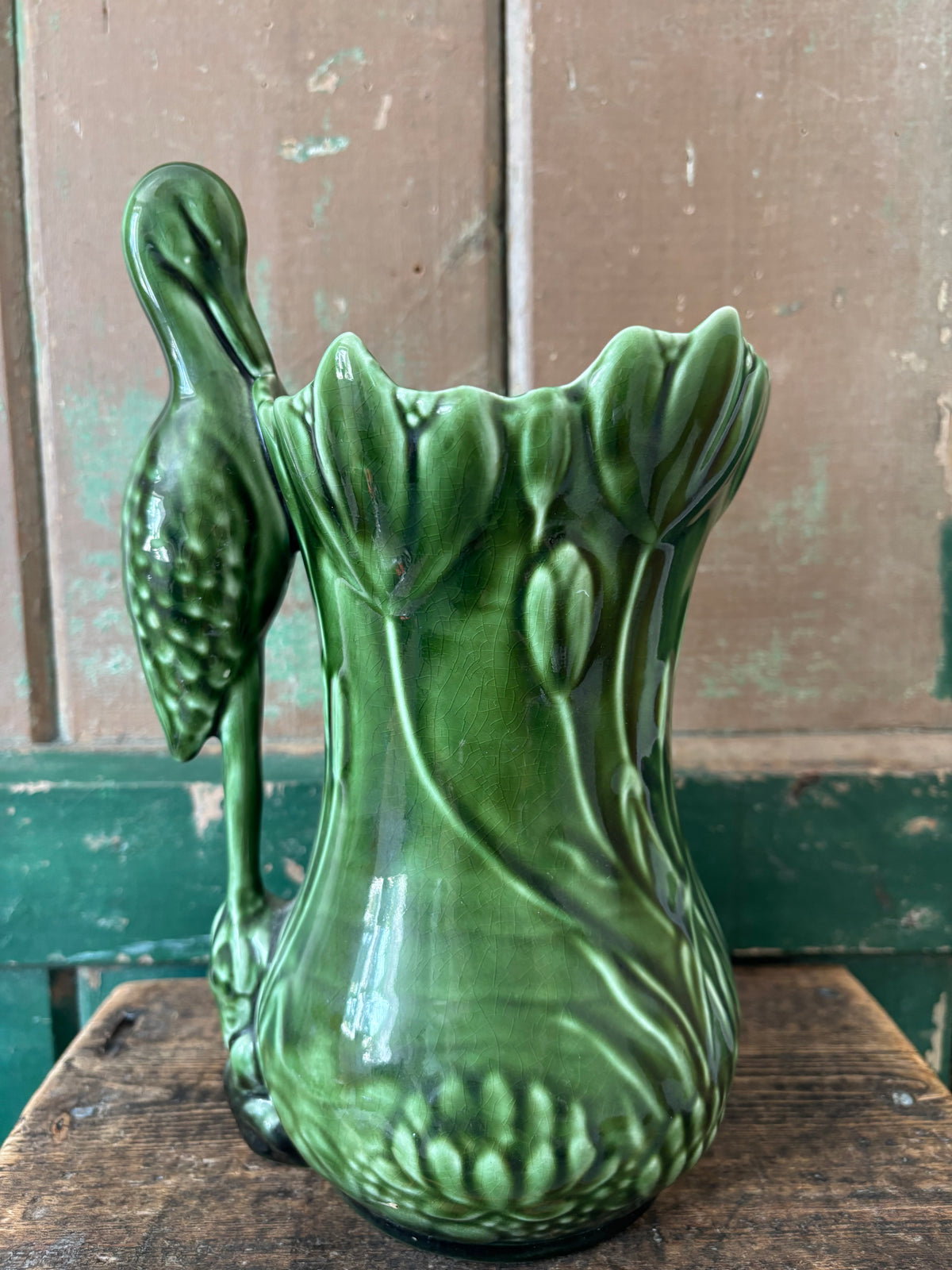 A dark green ceramic vase shaped like a lotus flower with a heron perched on the side.