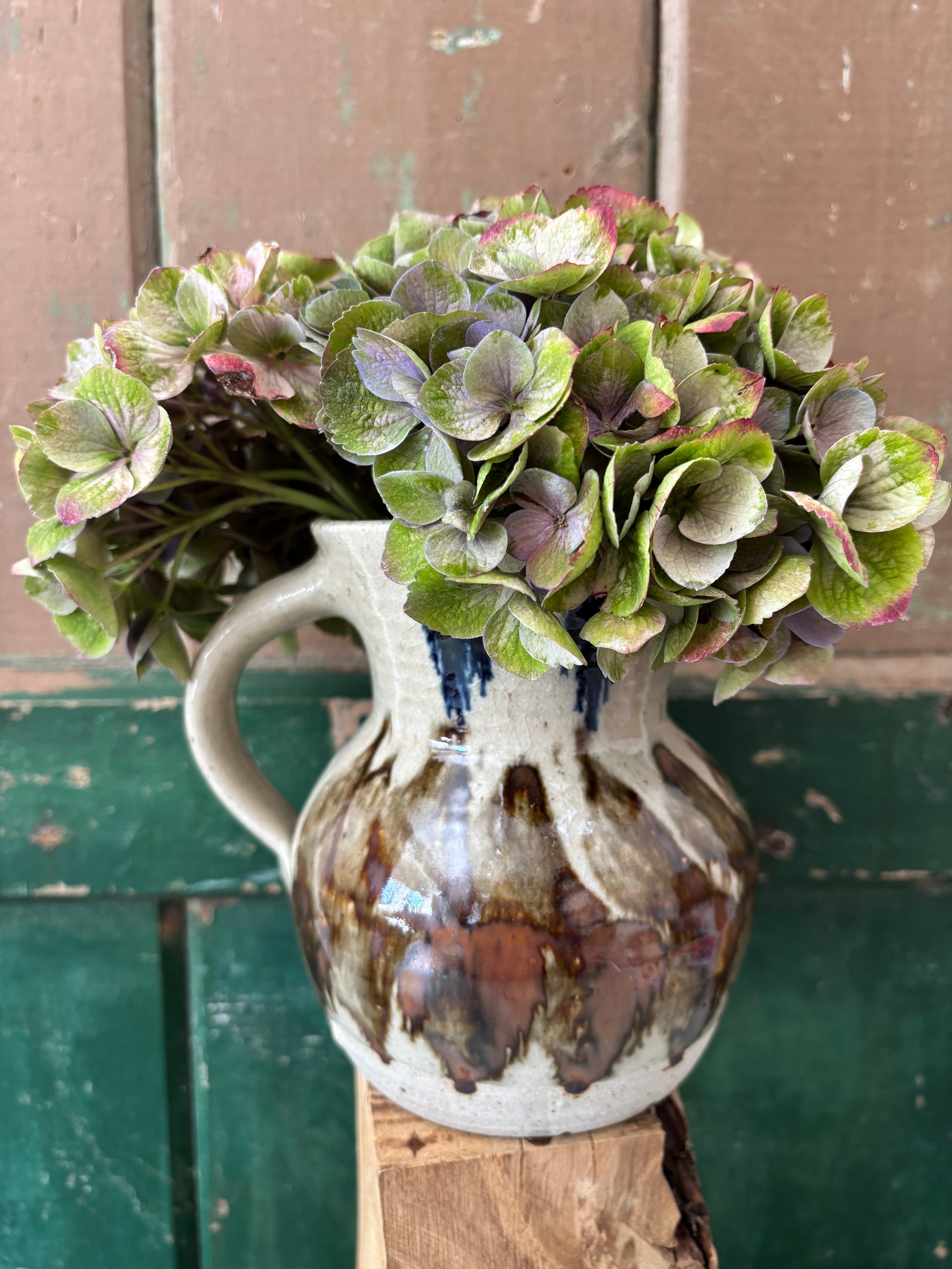 A ceramic pitcher vase with a handle, decorated in a speckled off-white glaze with brown and blue accents.