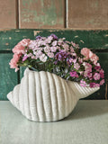 A vintage ribbed seashell-shaped planter holding pink and purple flowers.
