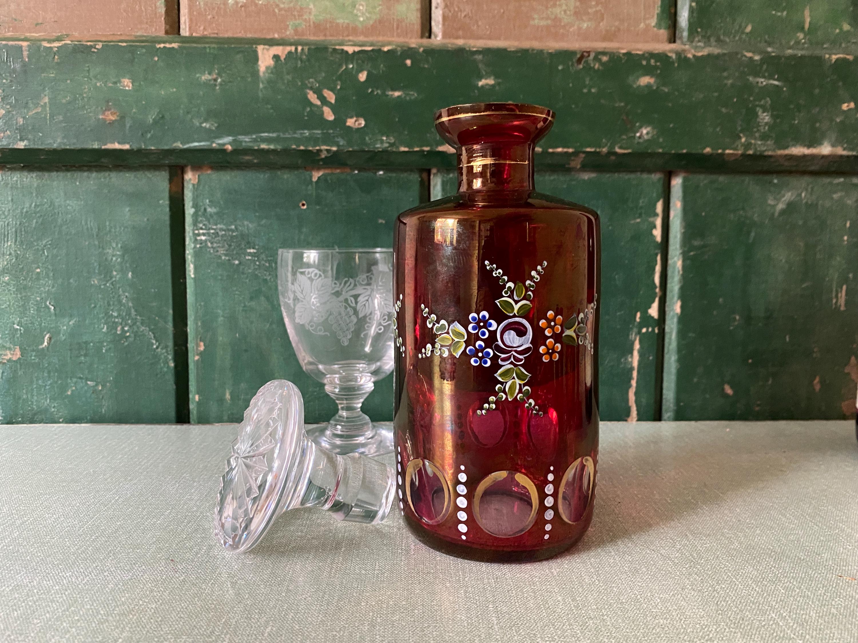 Red glass decanter with floral designs with a clear glass stopper and a wine glass