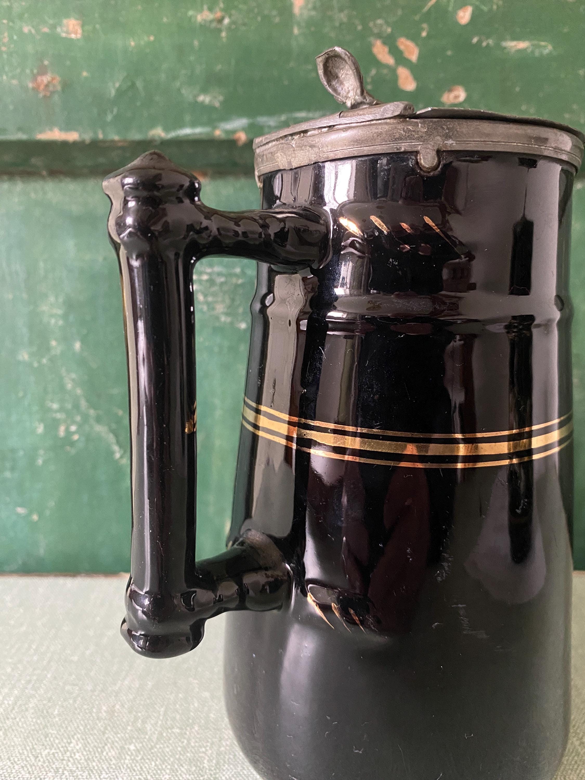 Detail of the handle of a black ceramic pitcher with gold stripe and hinged metal lid