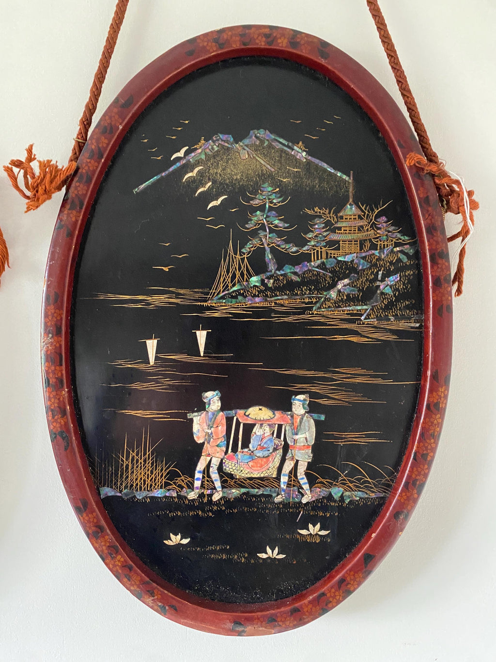 Decorative oval panel with a Japanese landscape scene and figures, in a red decorated frame