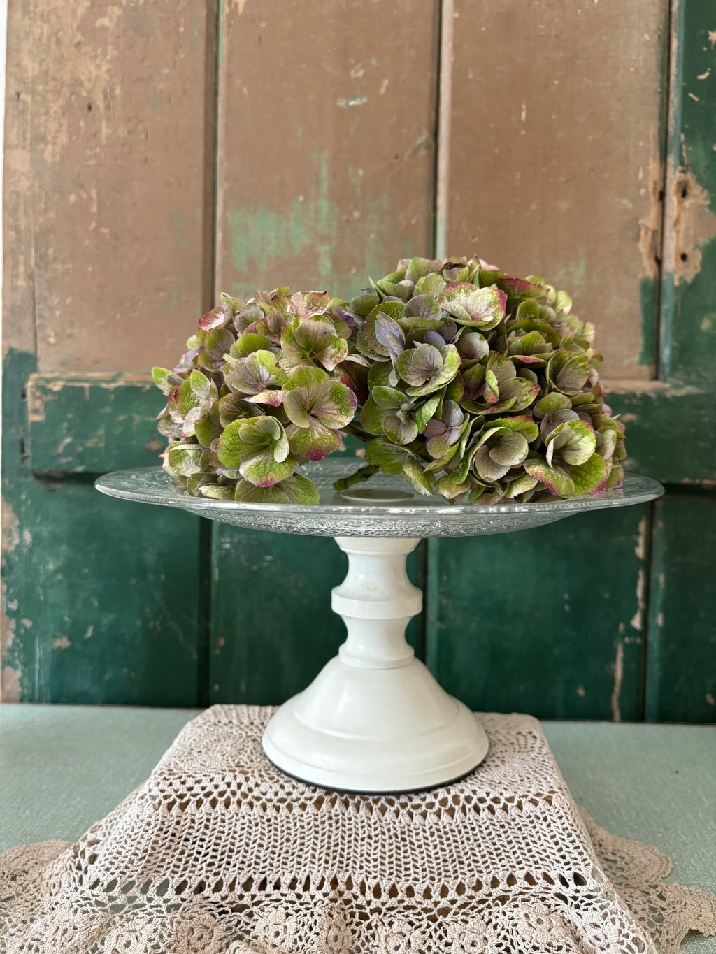  A cream pedestal cake stand with a clear glass top.