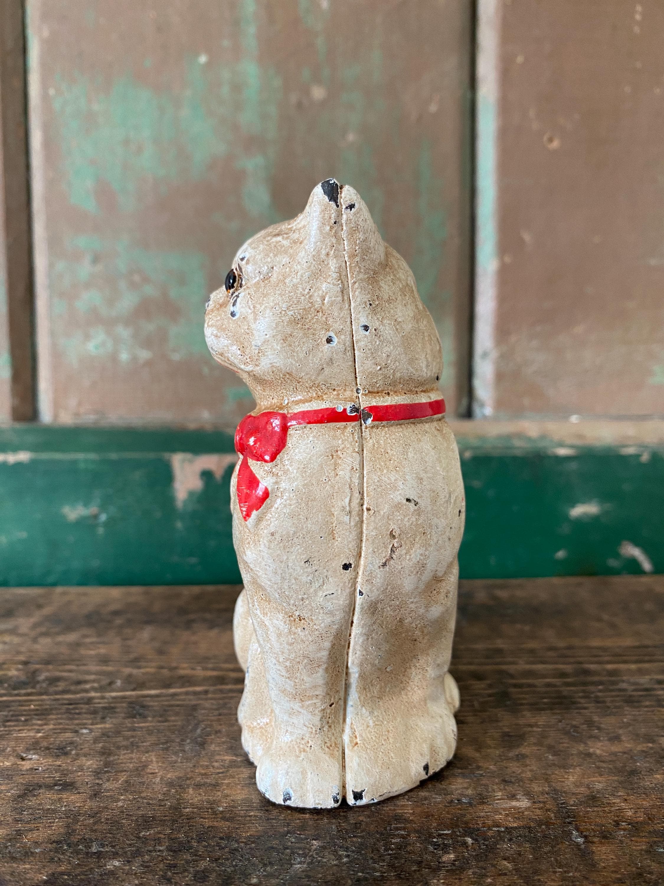 Side view of a small metal figurine of a white cat  with a red bow