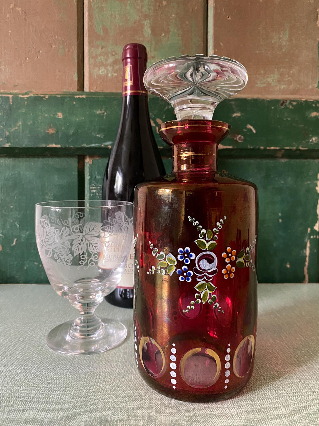 Decorative glass bottle with floral patterns next to a wine bottle and glass 
