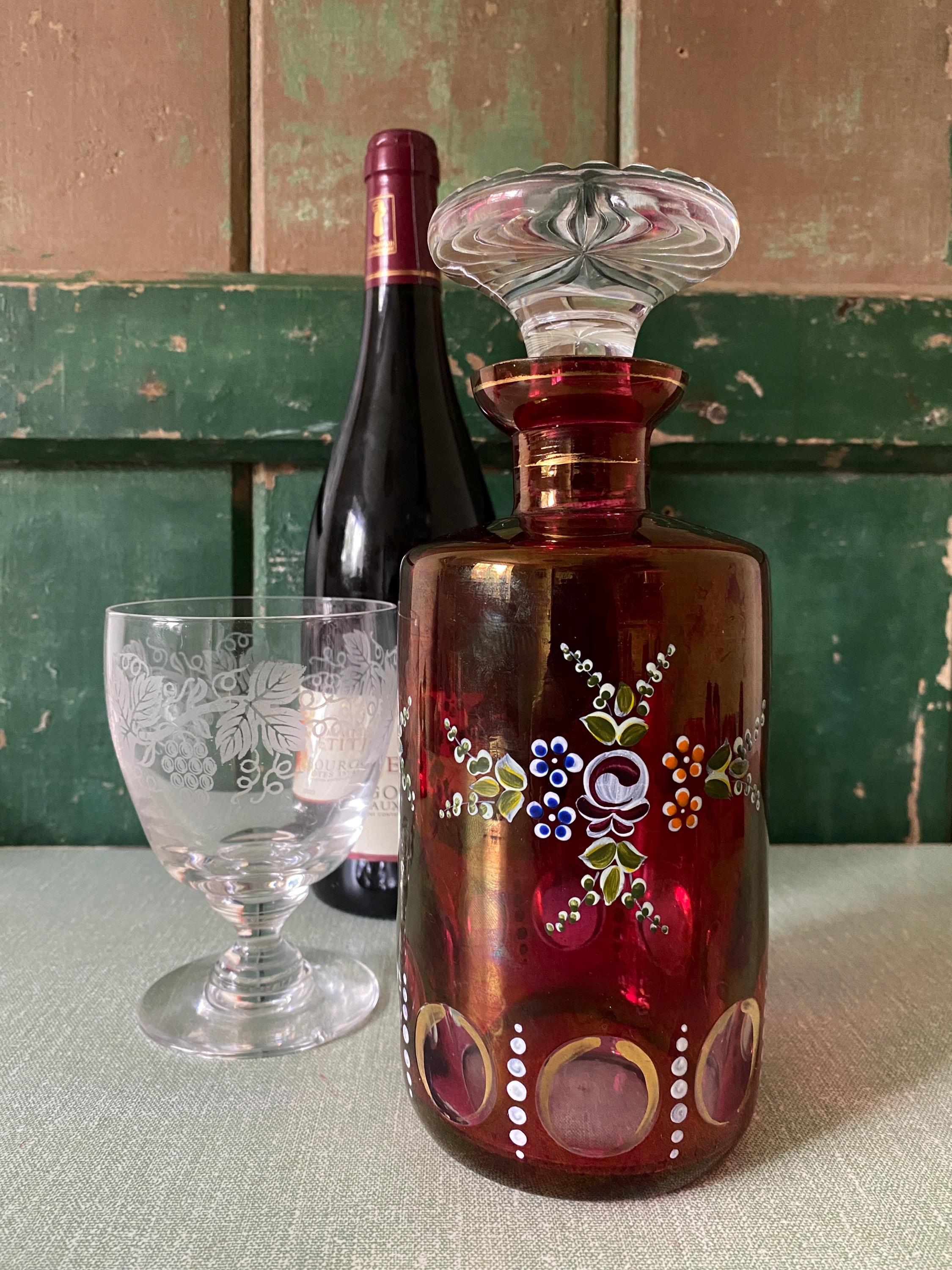 Decorative glass bottle with floral patterns next to a wine bottle and glass 