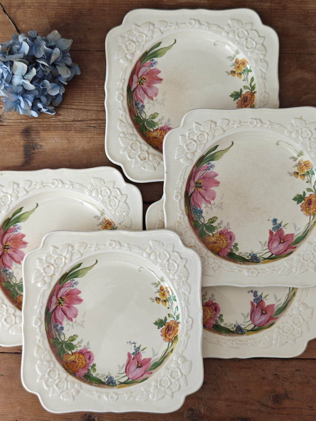 A set of five vintage cream ceramic plates with embossed floral borders and painted pink flowers.