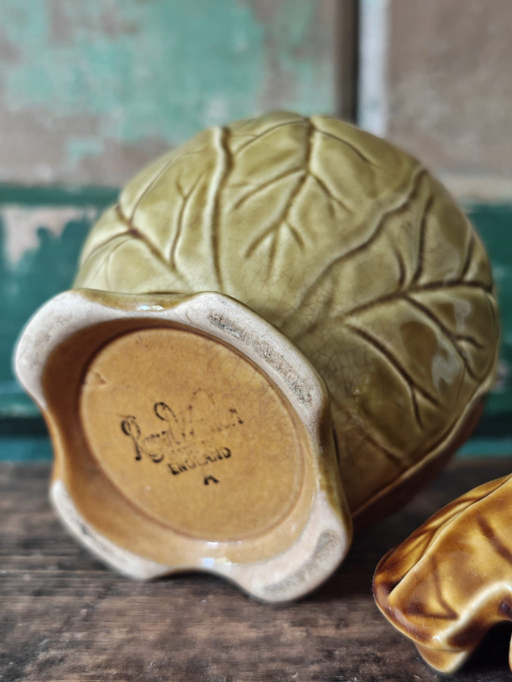 Close-up of the underside showing the makers mark of a ceramic lidded container with a leaf-like embossed pattern in a warm olive-gold glaze.