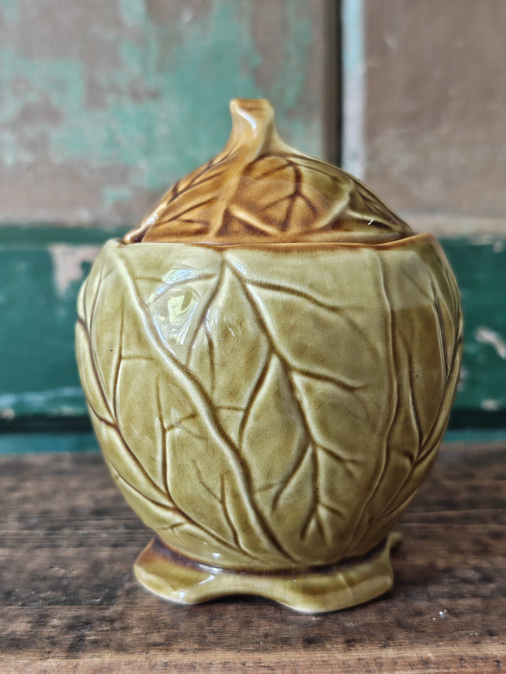 A ceramic lidded container with a leaf-like embossed pattern in a warm olive-gold glaze.