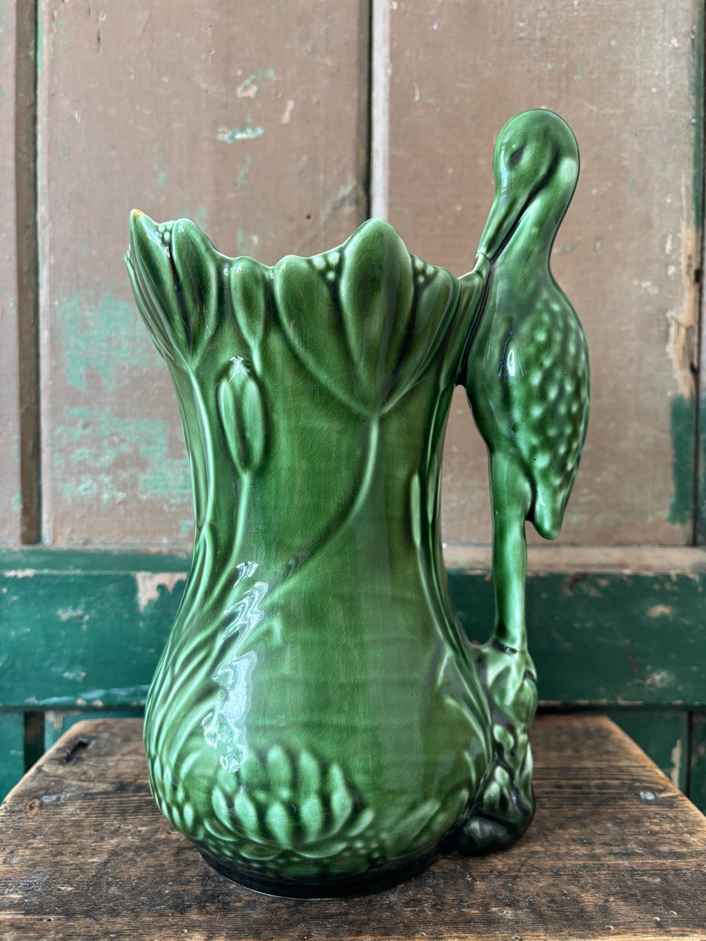 A dark green ceramic vase shaped like a lotus flower with a standing heron on the side.