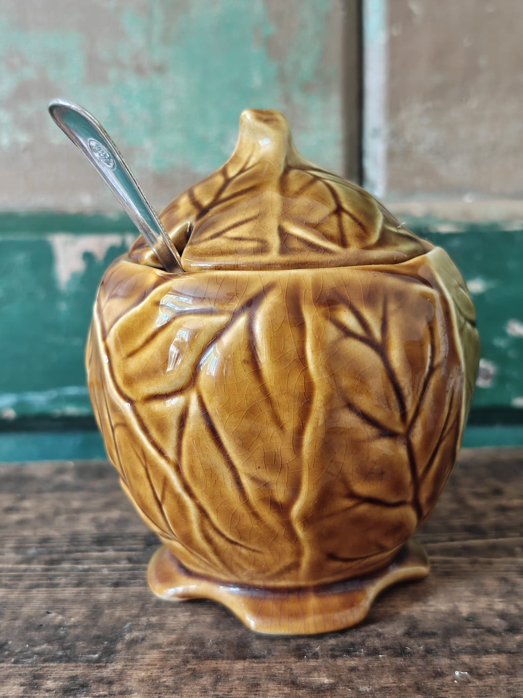 A ceramic lidded container with a leaf-like embossed pattern in a warm olive-gold glaze.