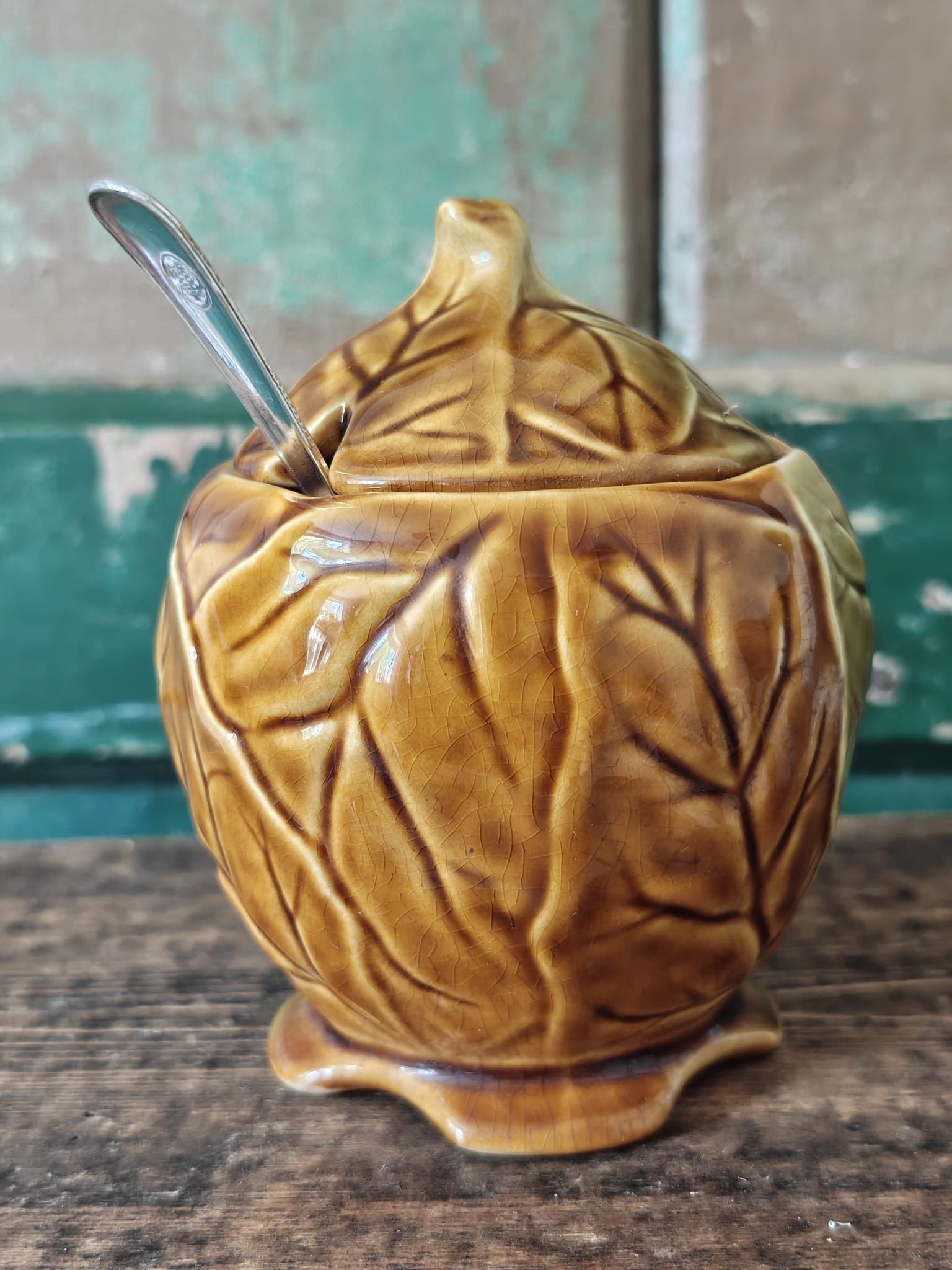 A ceramic lidded container with a leaf-like embossed pattern in a warm olive-gold glaze.