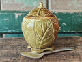 A ceramic lidded container with a leaf-like embossed pattern in a warm olive-gold glaze.